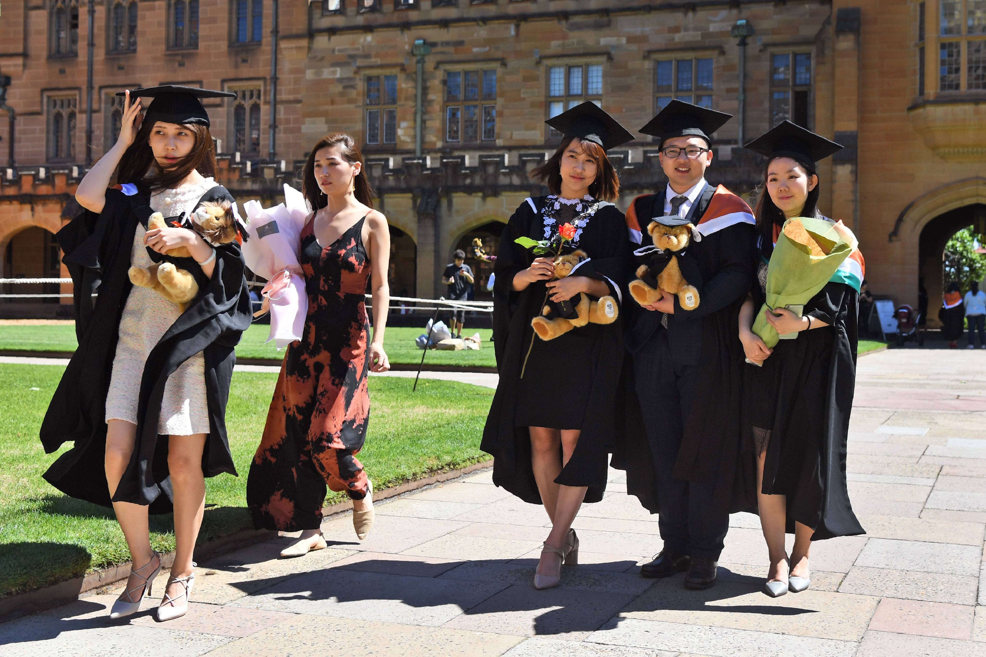 Students from China pose for family photos after graduating from a course in commerce at Sydney University on October 12, 2017. Families are rethinking sending their students to study abroad amid changed economic circumstances. Photo: AFP