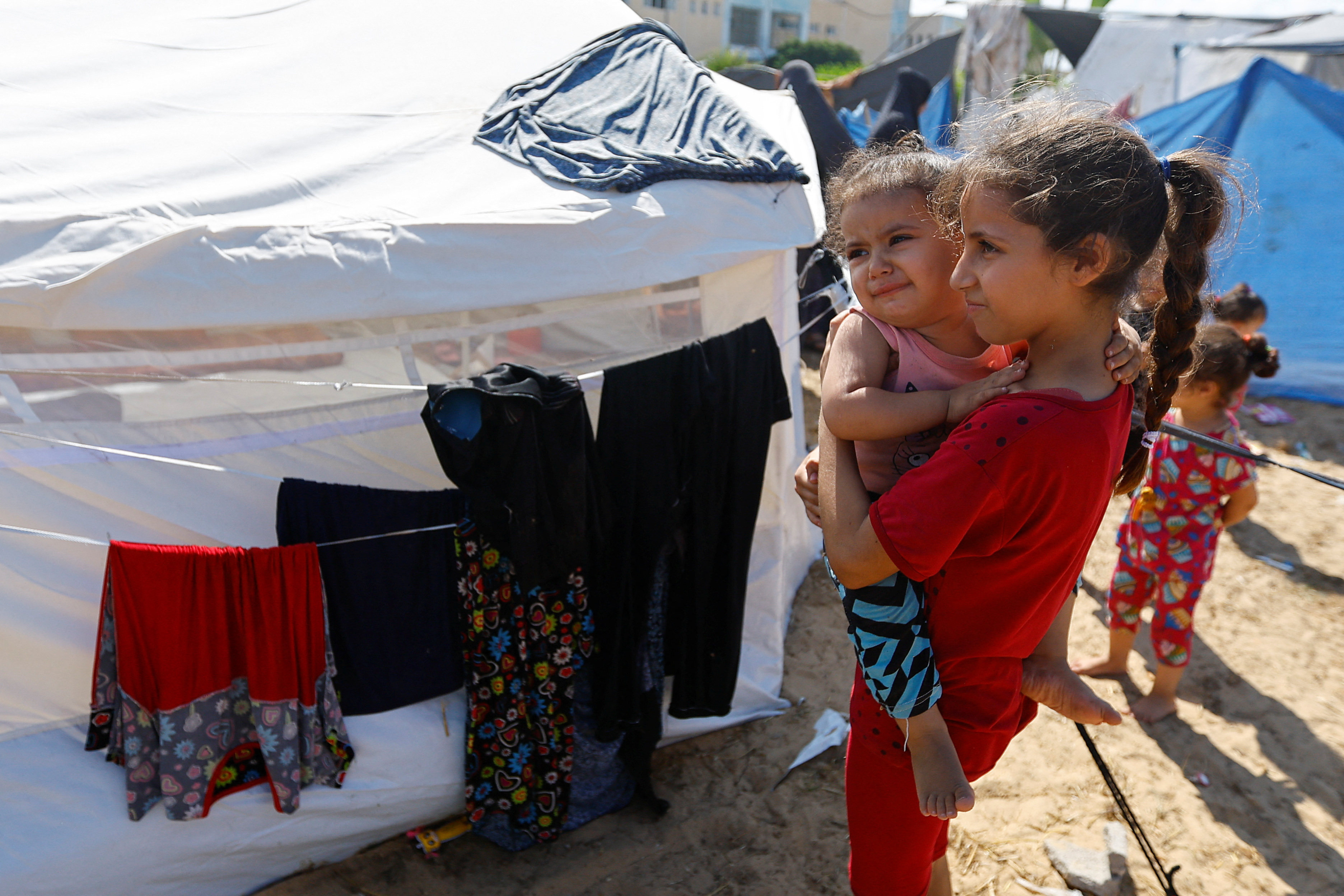 A Palestinian girl carries another girl after fleeing their house amid Israeli strikes, as they shelter at a United Nations-run centre in the Gaza Strip. Photo: Reuters