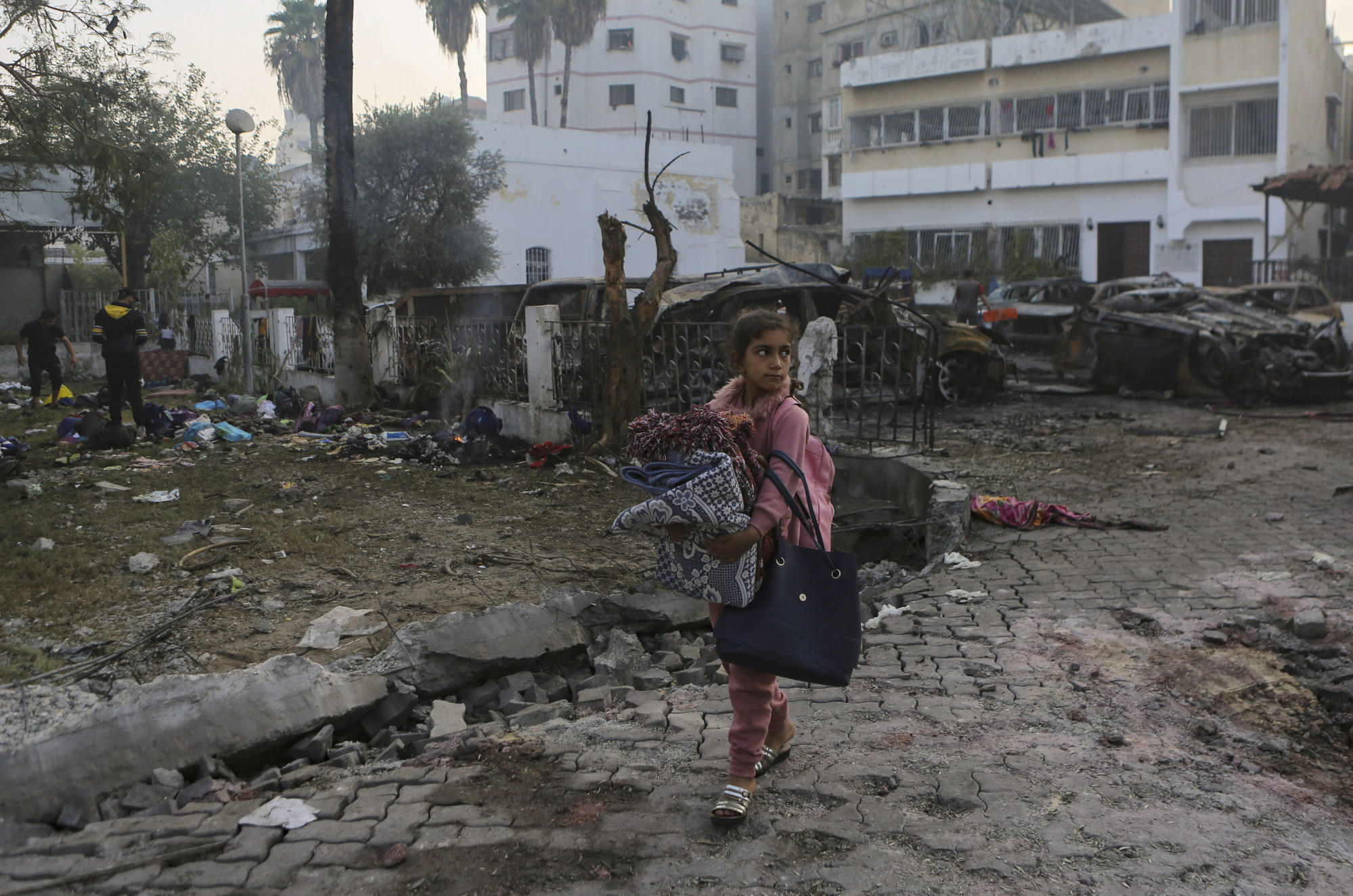 A Palestinian girl carries a blankets as she walks past the site of a deadly explosion at al-Ahli hospital in Gaza City on Wednesday. Photo: AP