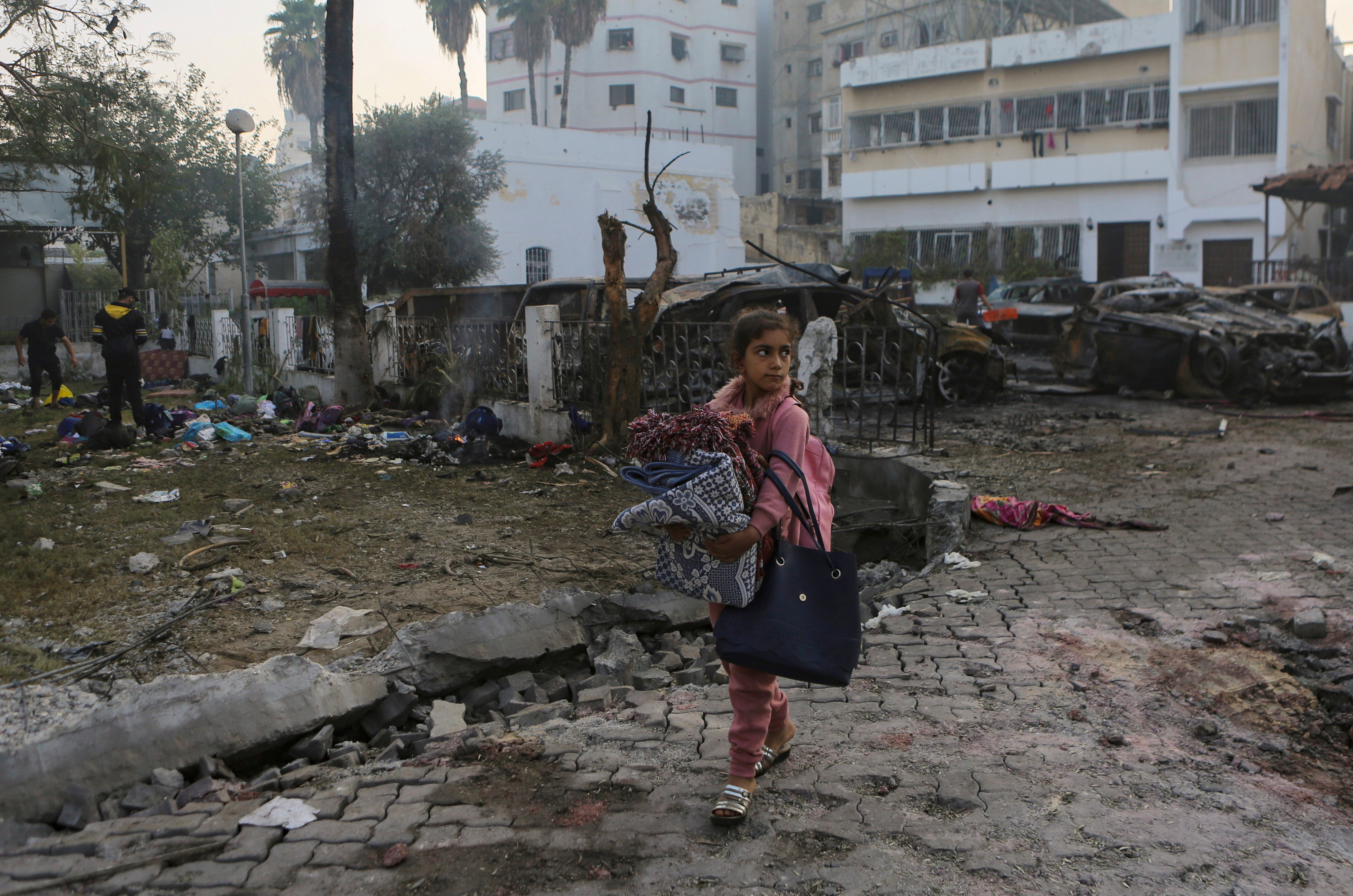 A Palestinian girl carries blankets as she walks past the site of a deadly explosion at the Al-Ahli Hospital in Gaza City on October 18. Photo: AP