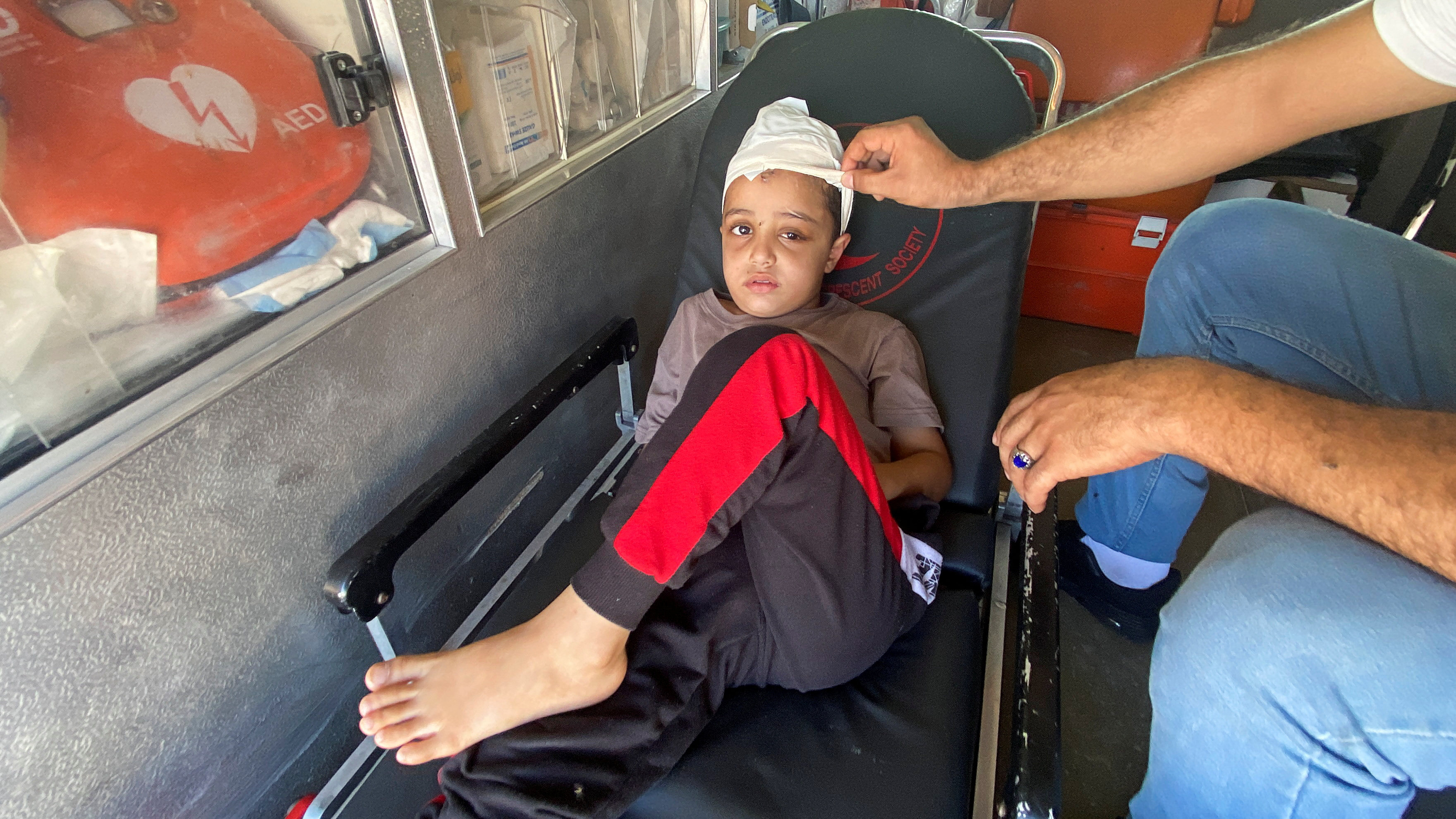 Palestinian boy Ameer Joma, who was injured in an Israeli strike on Gaza, sits with his father in an ambulance at the Rafah crossing, waiting to be transported to Egypt for treatment. Photo: Reuters

