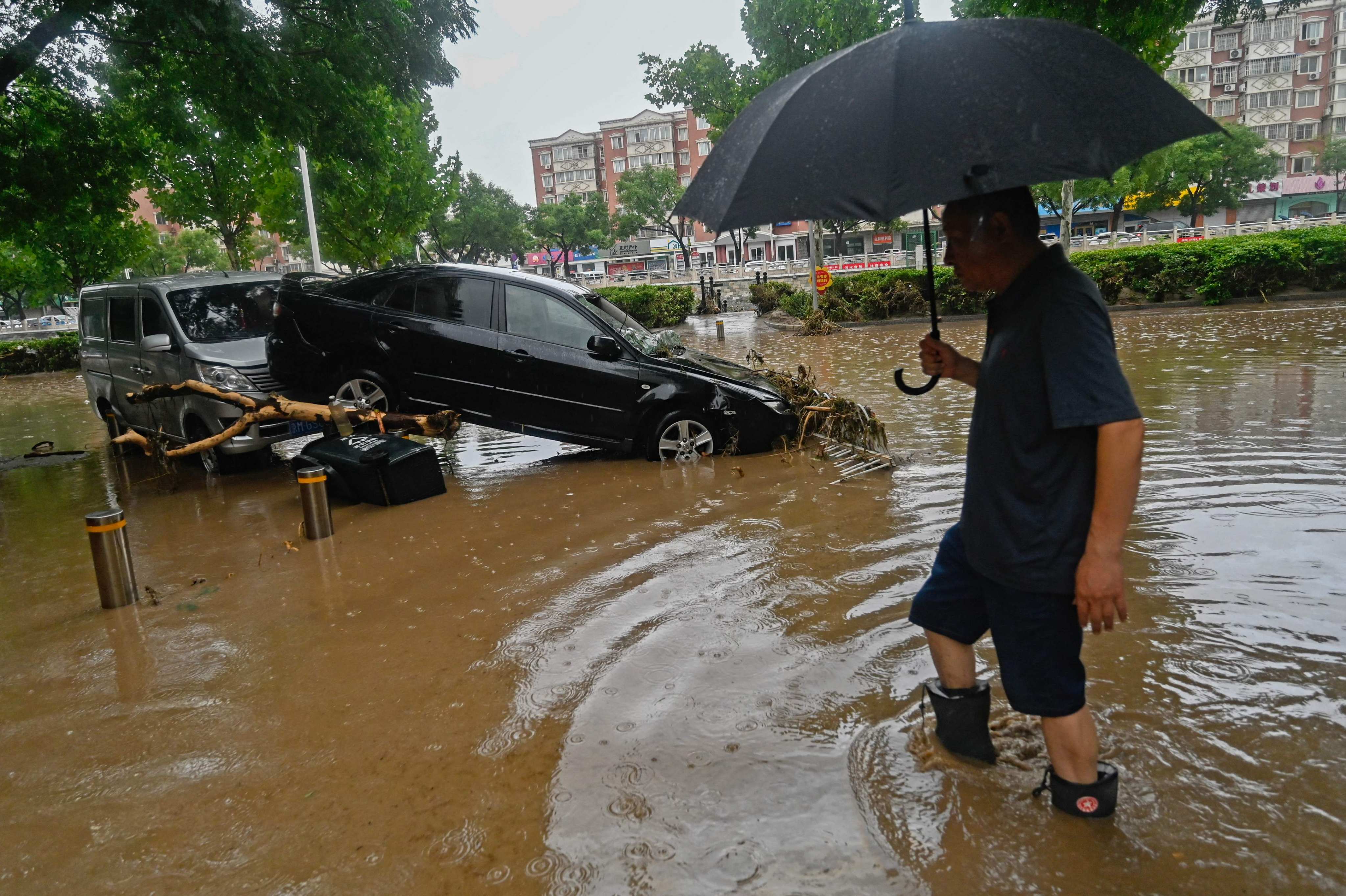 A man wades past a damaged car along a flooded street, after heavy rains in Mentougou district in Beijing. Photo: AFP