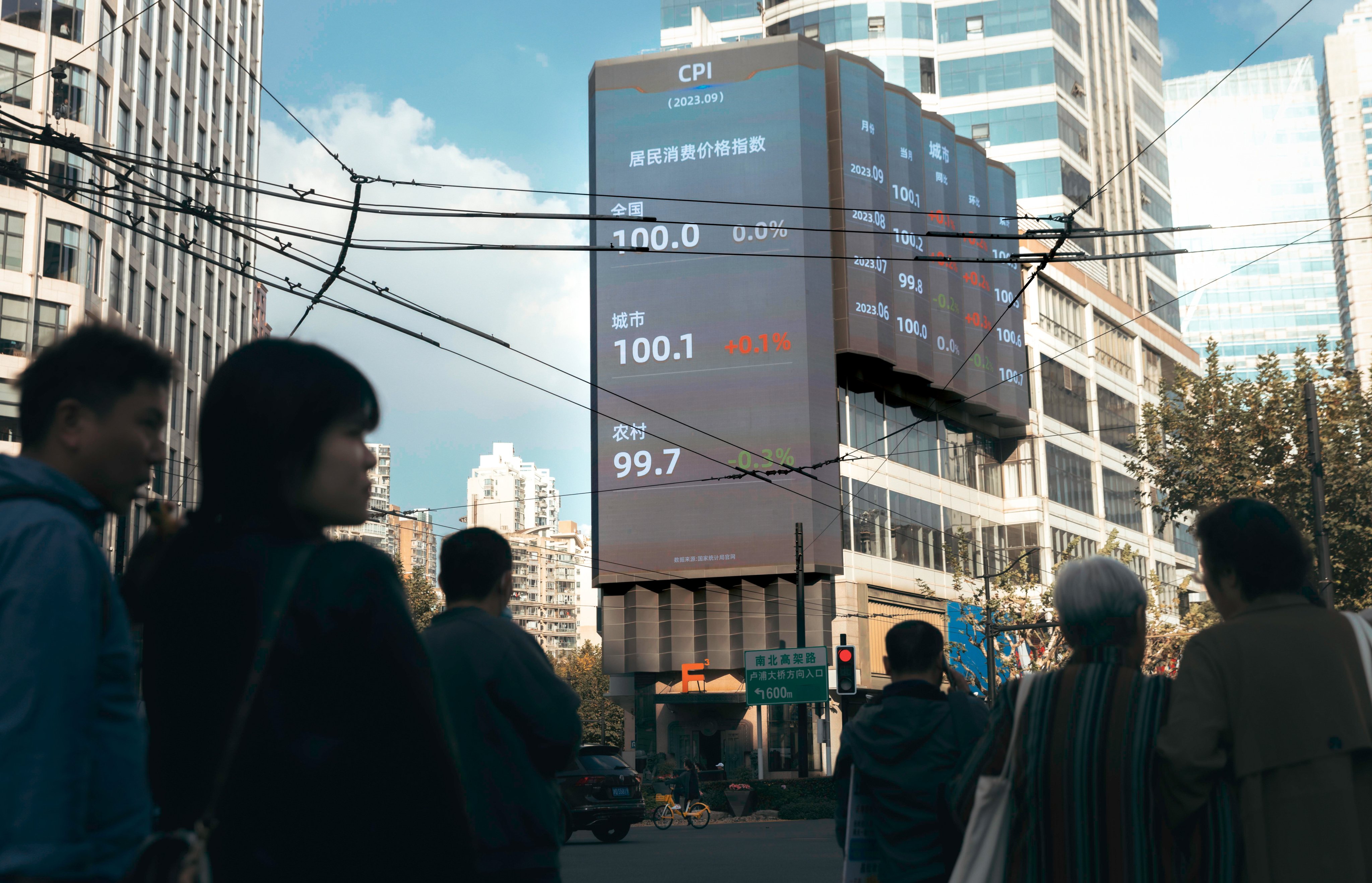 People stand on the street beneath a large screen showing the latest market and economic data, in Shanghai on October 20. Photo: EPA-EFE