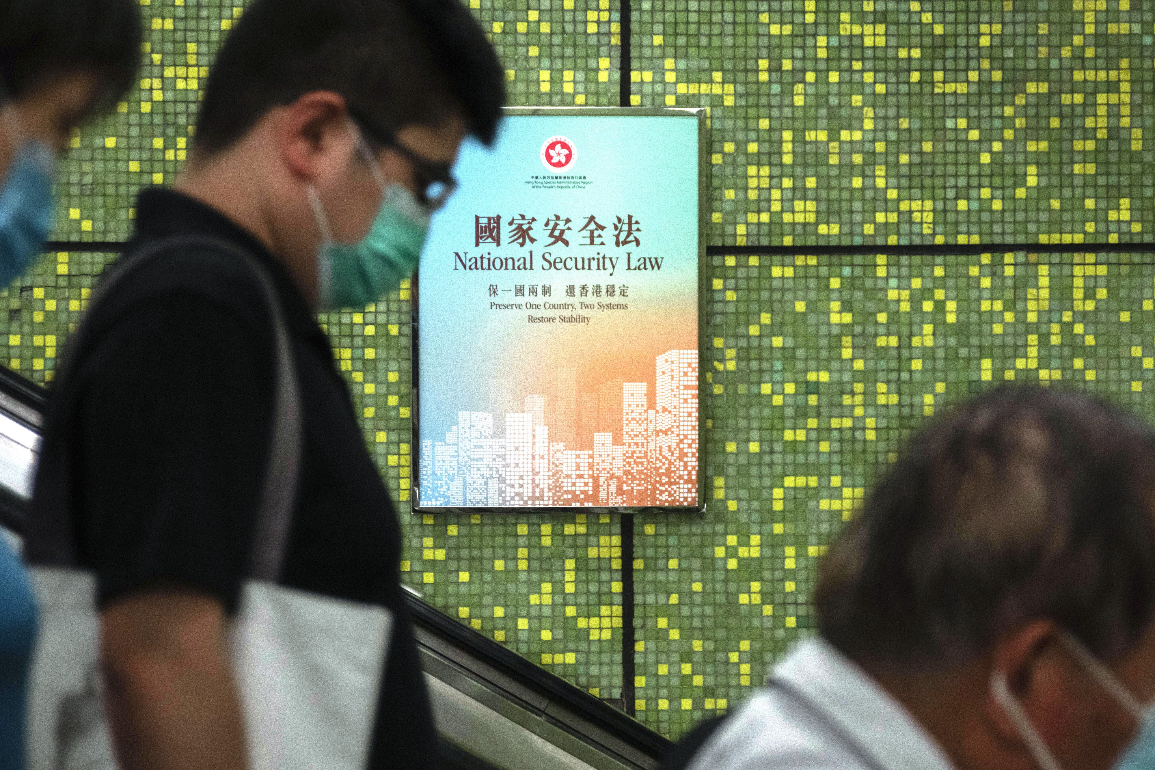 Pedestrians ride an escalator past a poster promoting the national security law poster in Wan Chai MTR station on July 2, 2020. Photographer: Bloomberg
