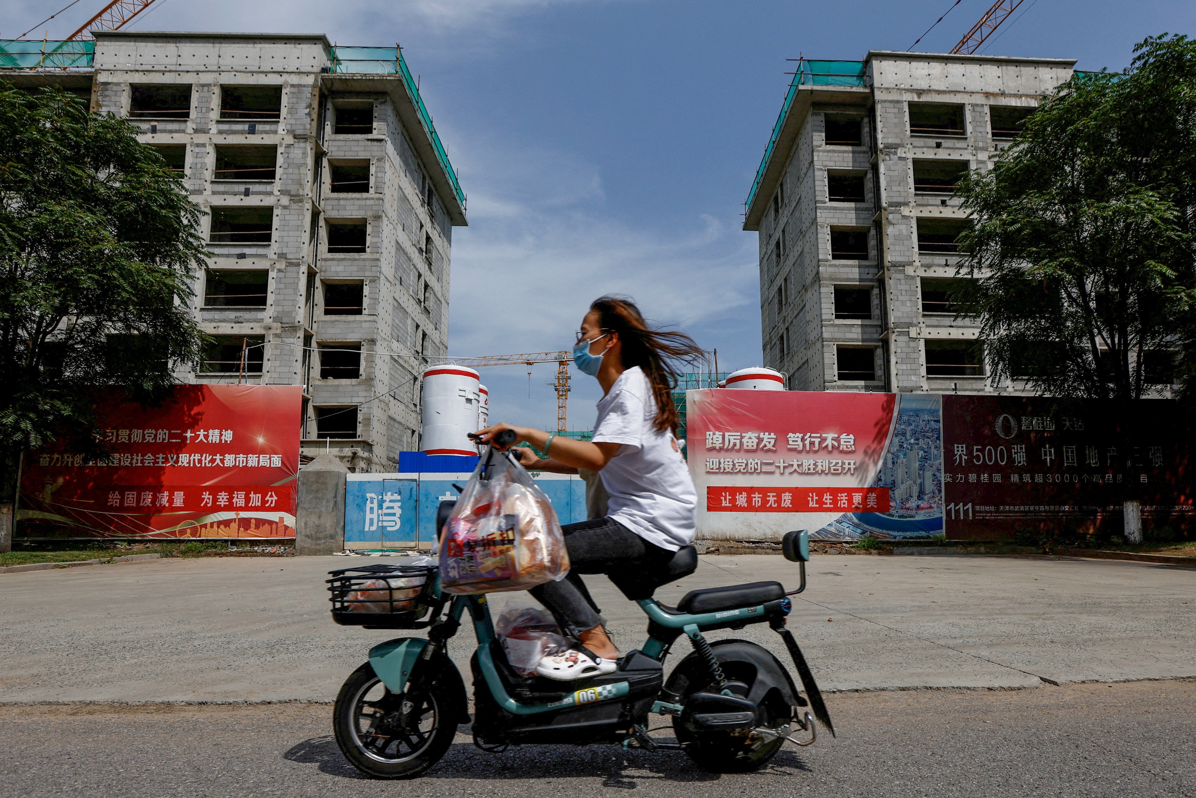 A woman rides a scooter past a construction site in Tianjin on August 18. China is busy dealing with its “twin cancers”: a property bubble and shadow banking system rife with Ponzi schemes. Photo: Reuters