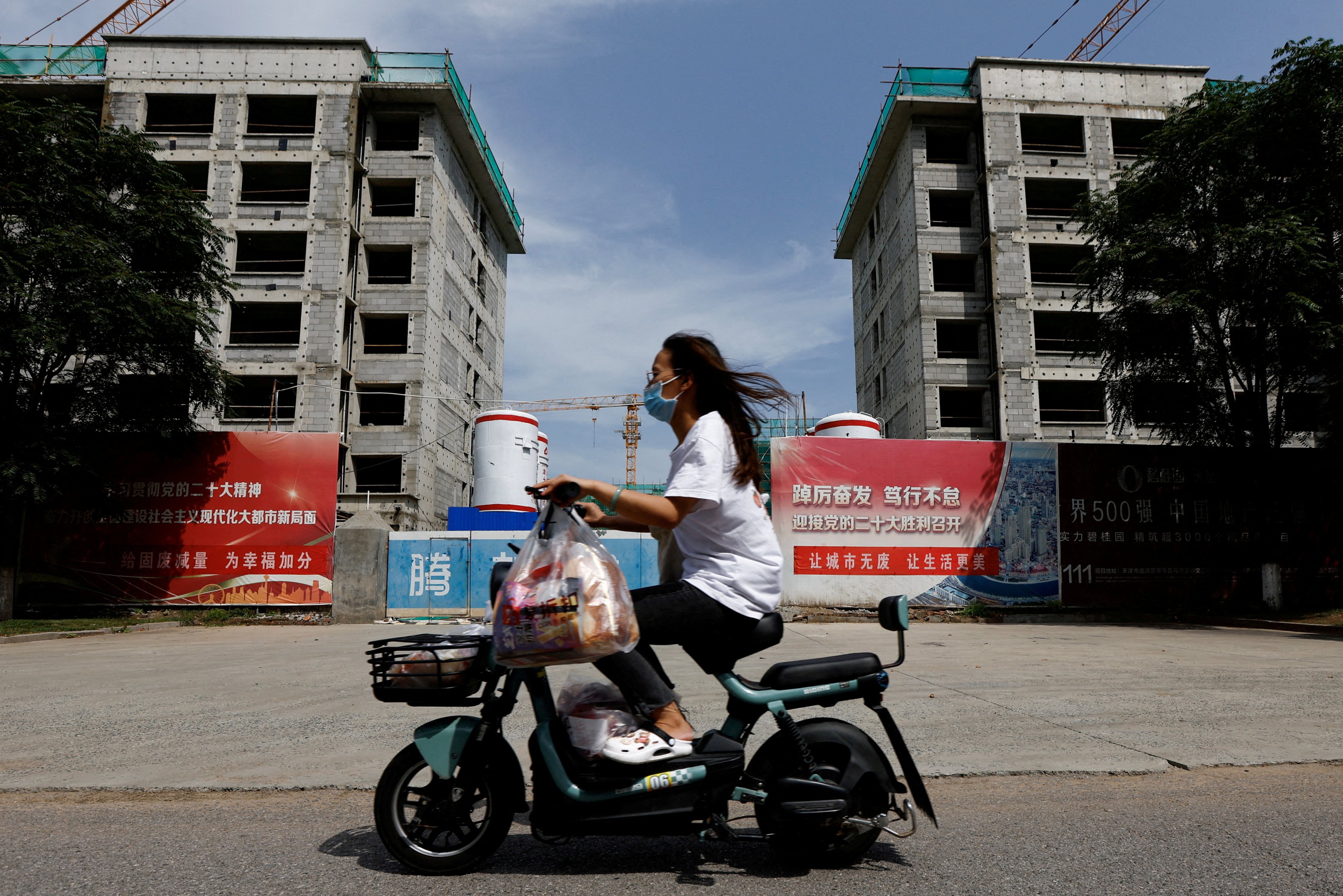 A woman rides a scooter past a construction site for residential buildings by indebted Chinese developer Country Garden in Tianjin on August 18. Photo: Reuters