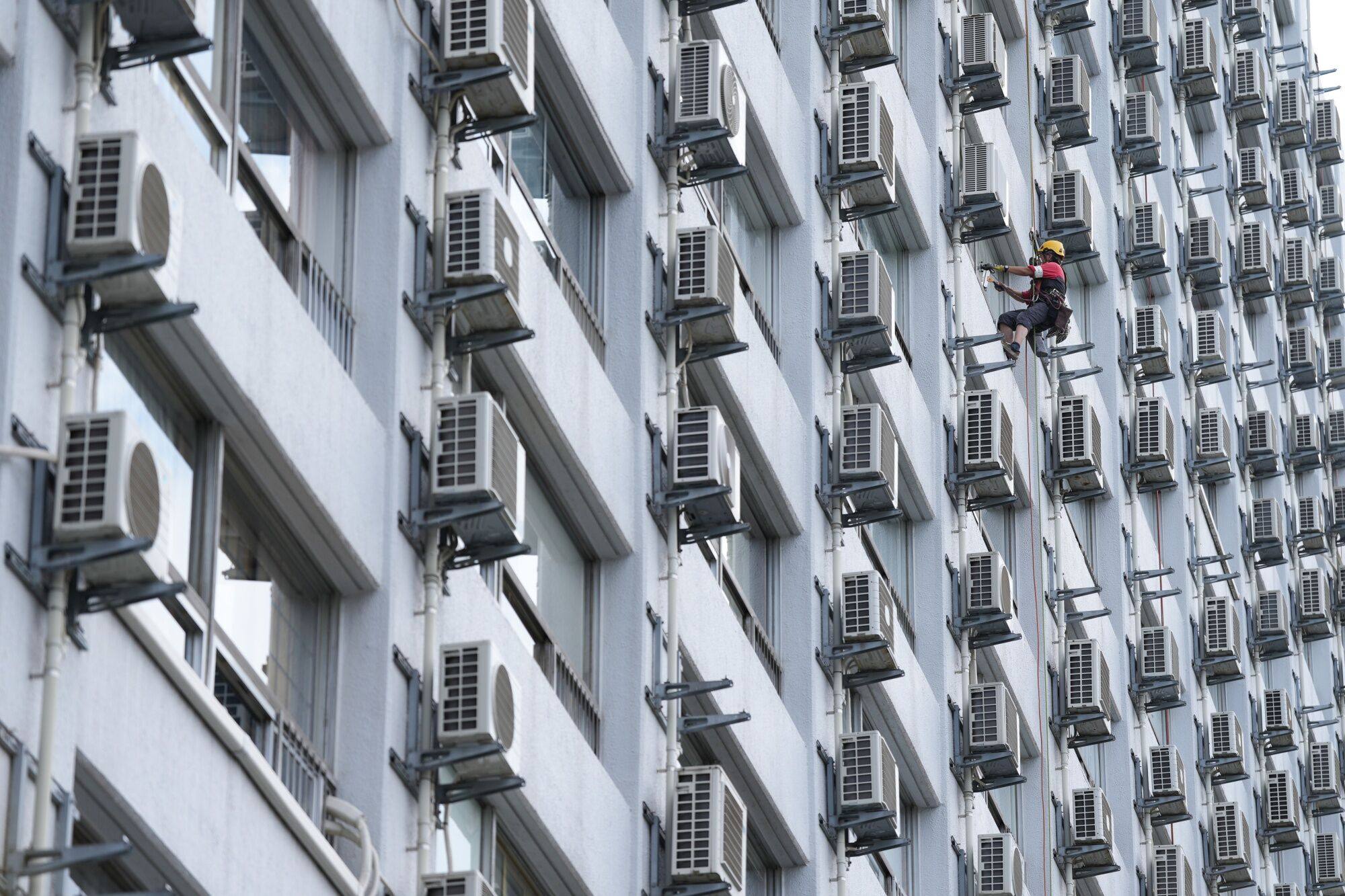 A worker washes windows next to air conditioning units at an apartment building in Tokyo, Japan, on July 21. Flat prices in the capital have risen sharply, leaving them on a par with their level at the peak of the asset price bubble. Photo: Bloomberg