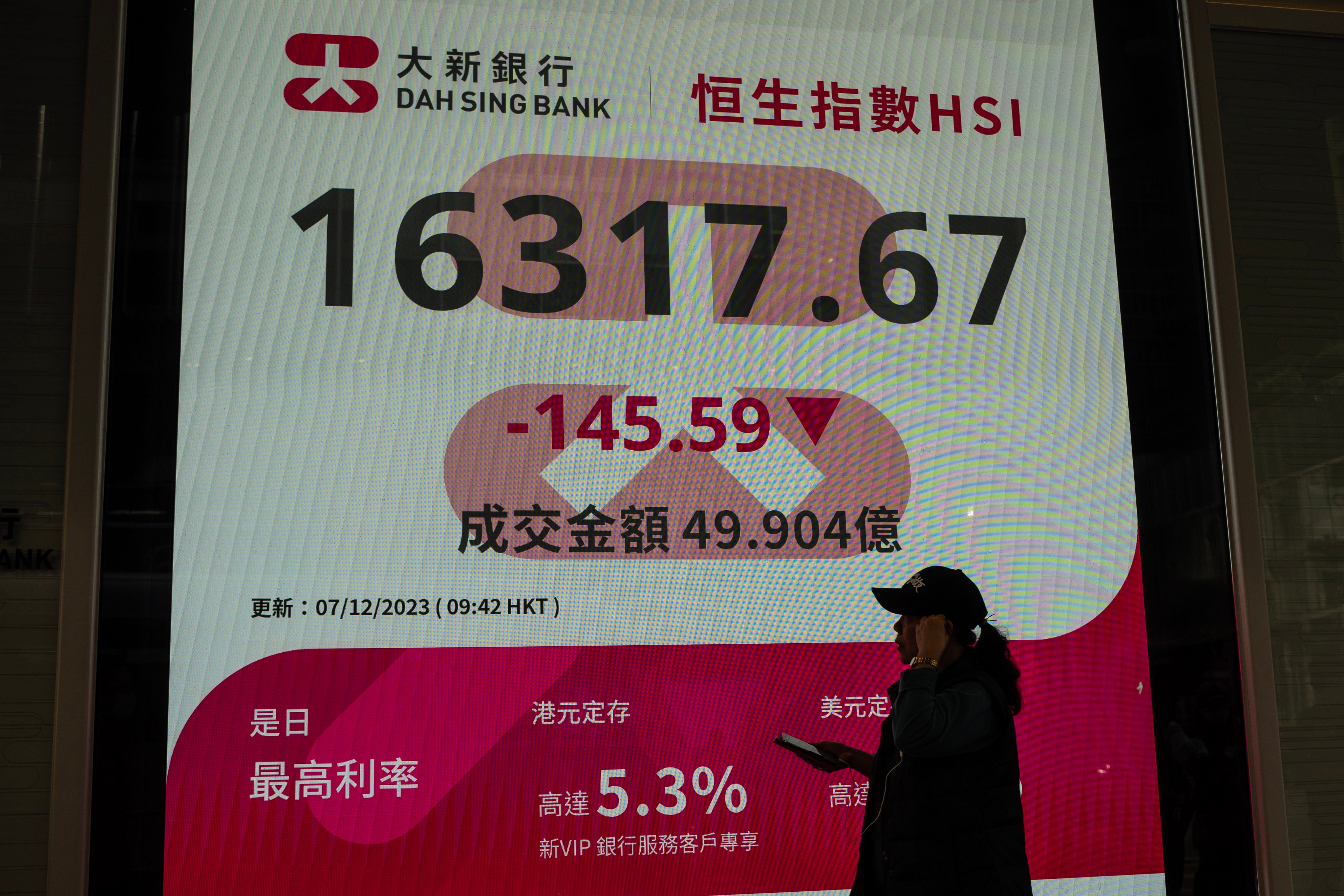 A woman walks past an electronic display showing the Hang Seng Index in Hong Kong, December 7, 2023. Photo: NurPhoto via Getty Images