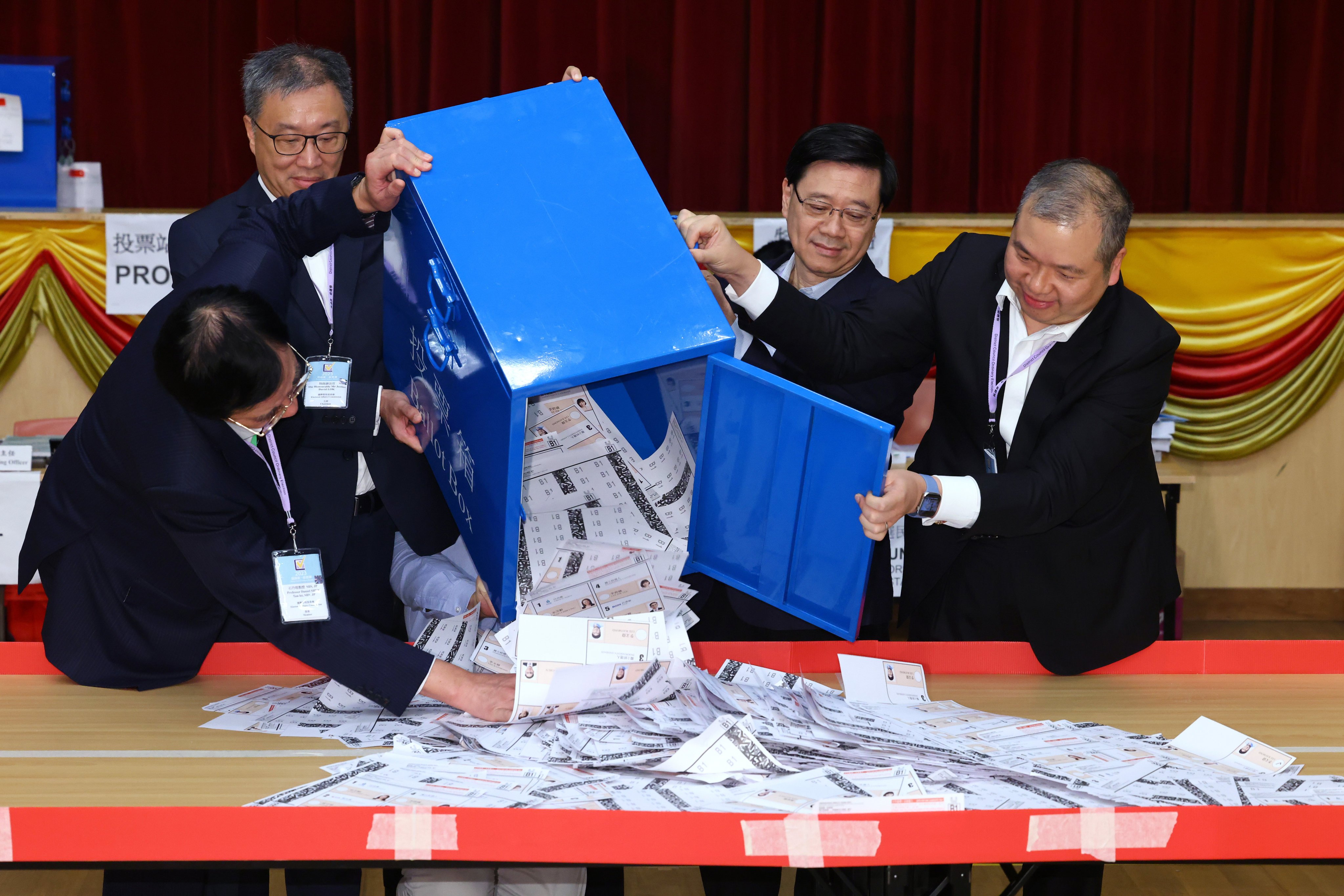 Chief Executive John Lee Ka-chiu (second right) looks on as Electoral Affairs Commission members empty a ballot box in the counting station for the district council election at Queen’s College in Causeway Bay on December 11. Photo: Dickson Lee