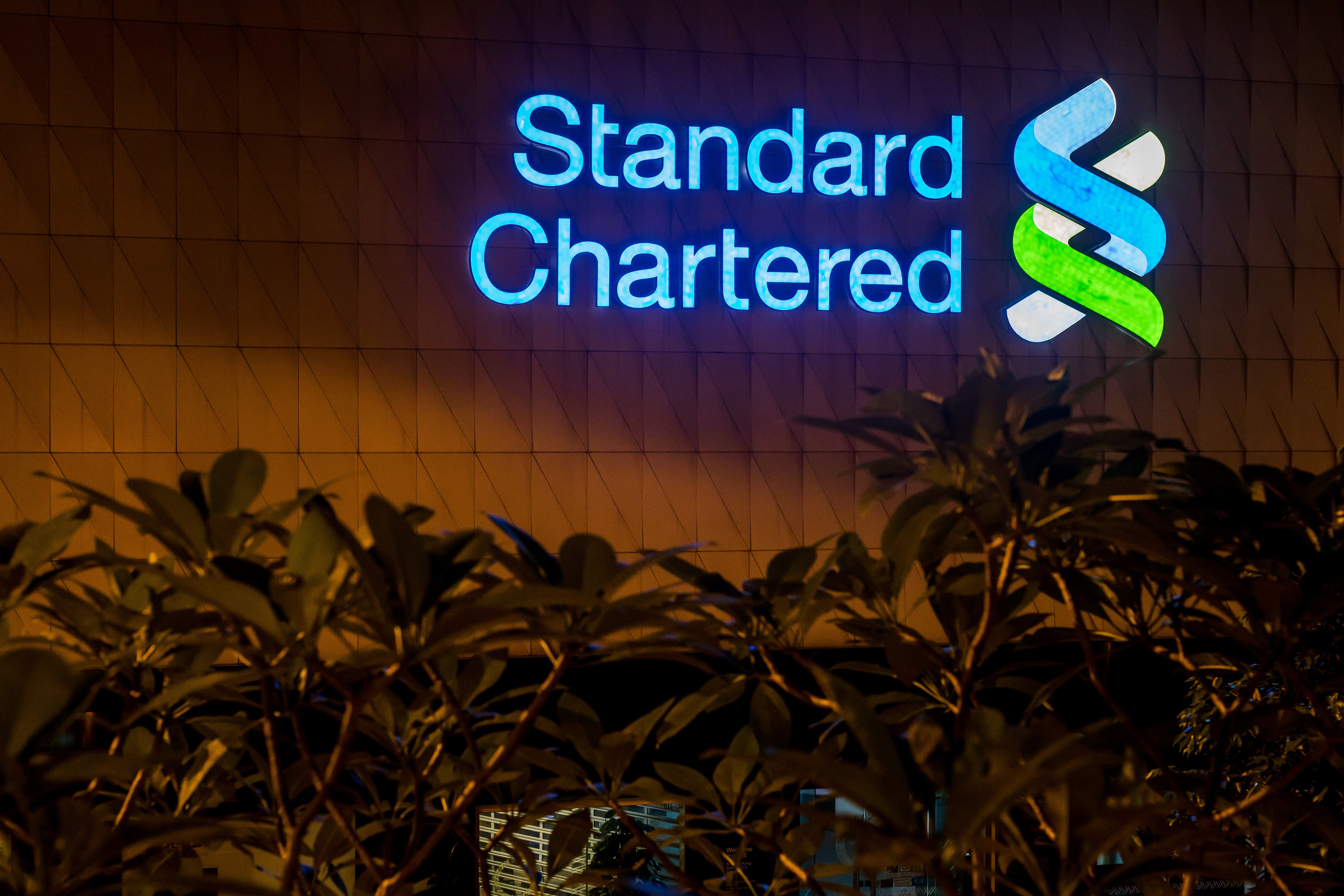 Signage is illuminated atop a Standard Chartered Plc bank branch at night in Hong Kong, China. Photo: Bloomberg