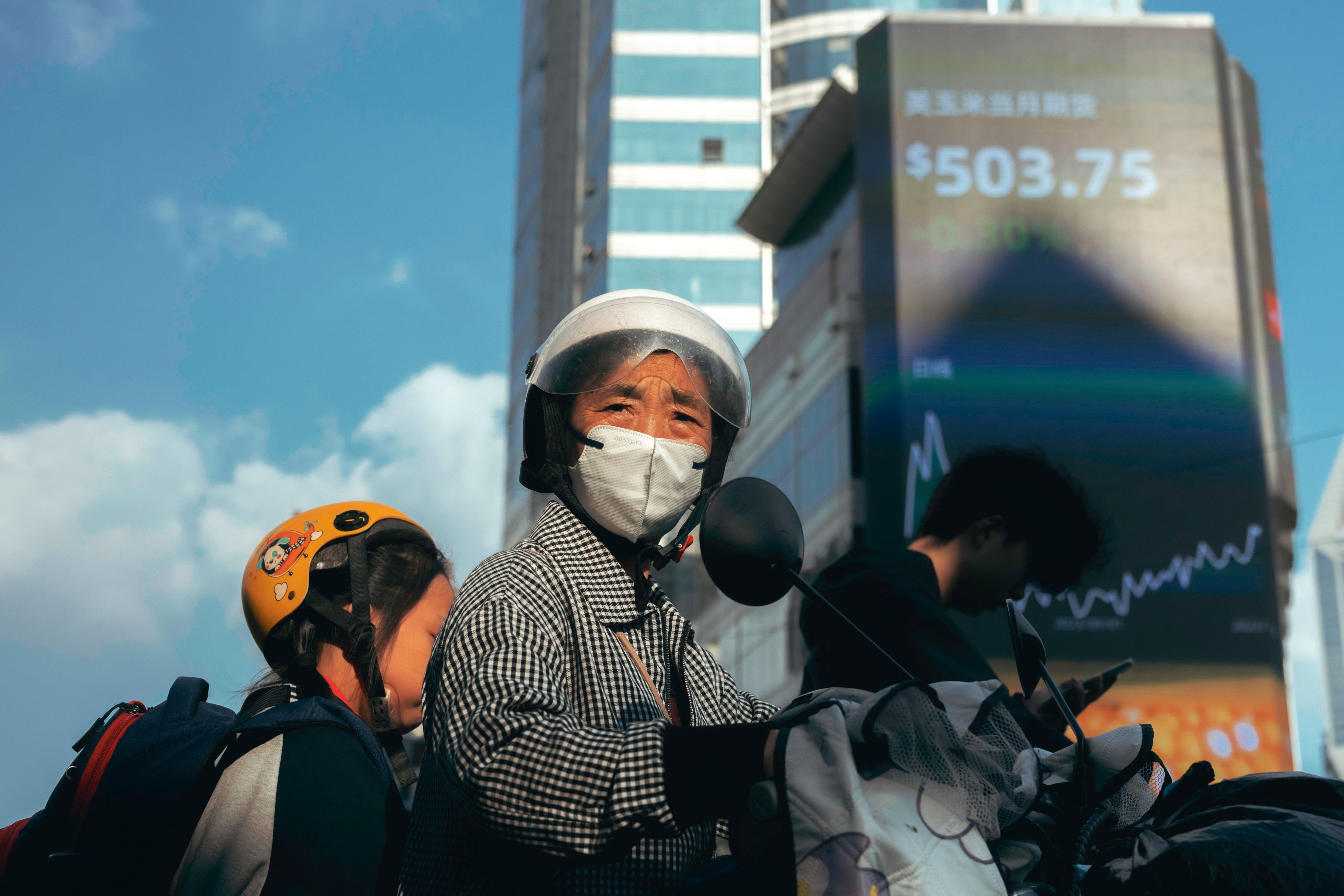 A woman rides a scooter beneath a large screen showing stock exchange and economy data in Shanghai on October 20, when Asian shares hit an 11-month low.  Photo: EPA-EFE