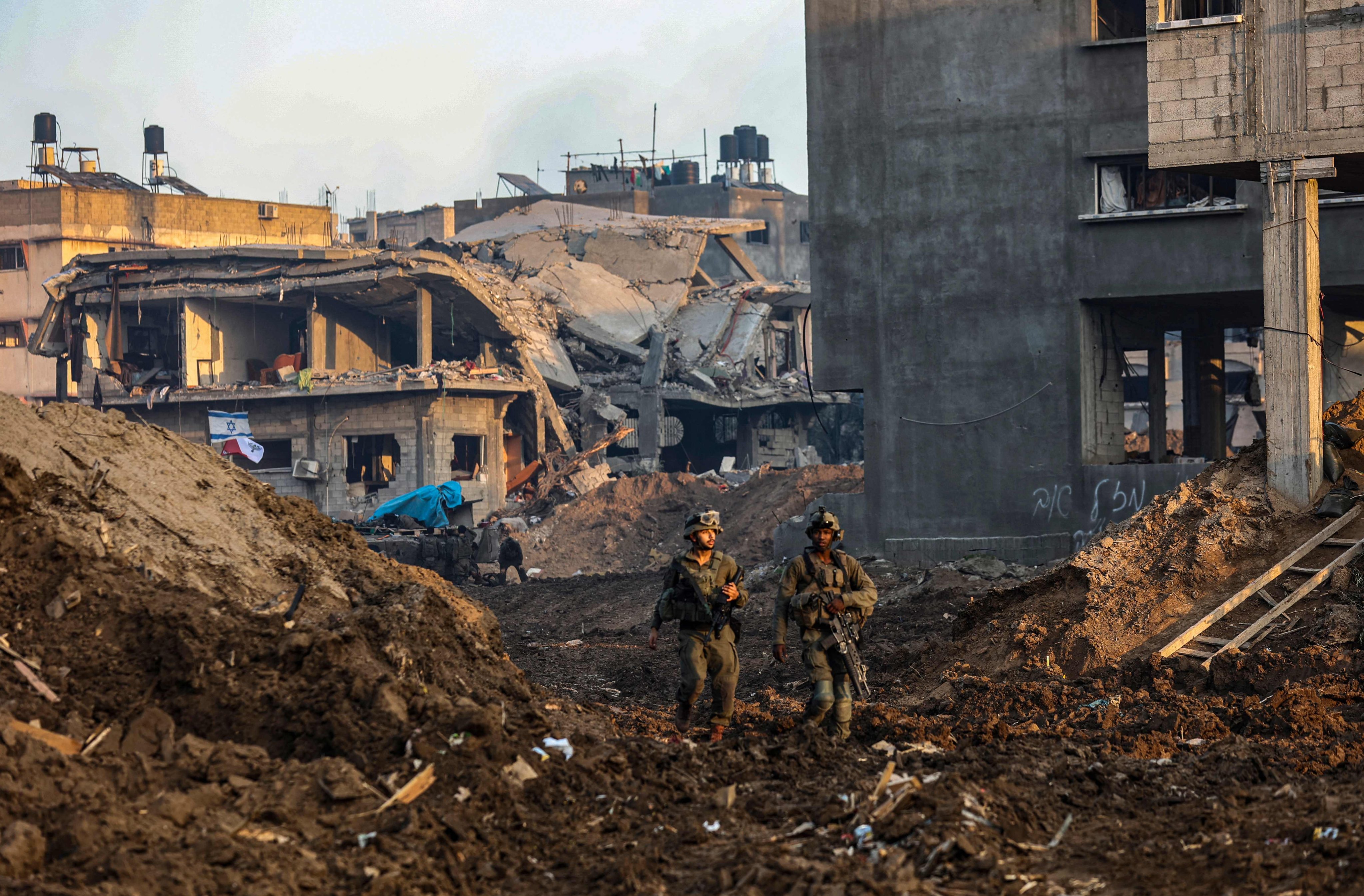 Israeli soldiers walk past damaged buildings during a military operation in the north of the Gaza Strip amid continuing battles between Israel and Hamas on December 19. This photo was taken during a controlled tour and subsequently edited under the supervision of the Israeli military. Photo: AFP