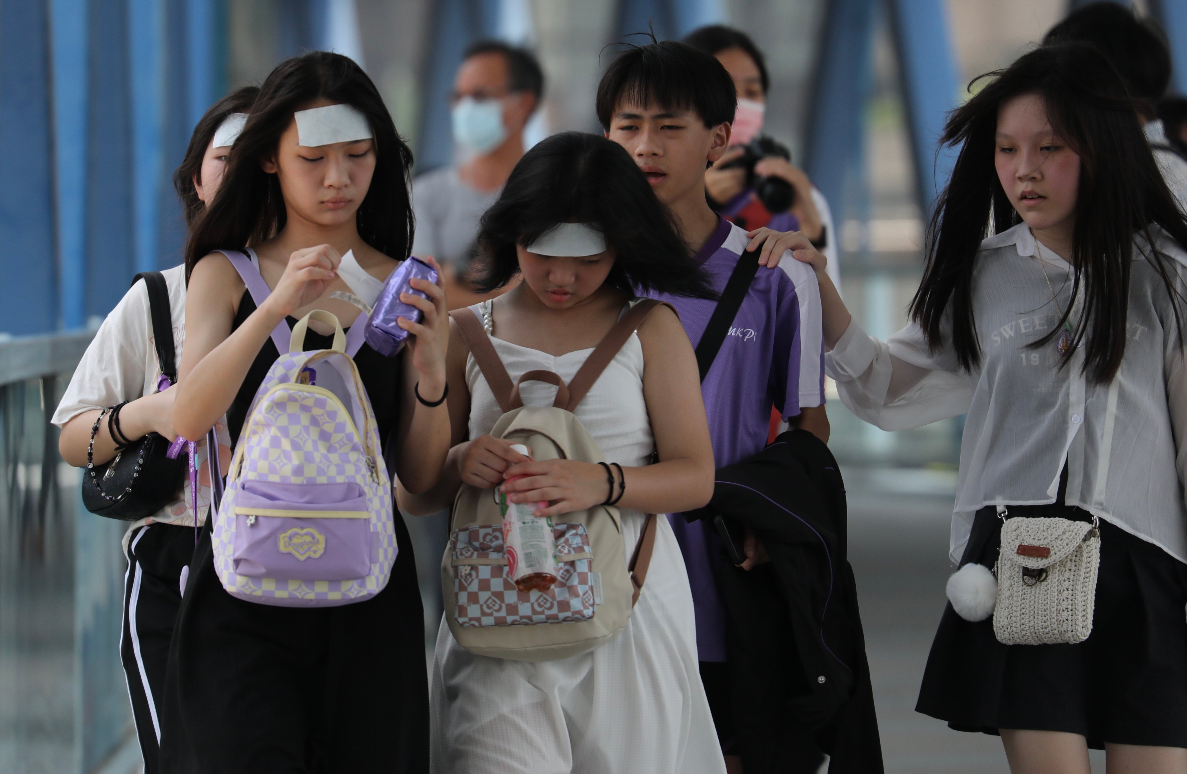 Pedestrians walk down a footbridge, in Central, Hong Kong, with cooling pads on their foreheads during a hot day in June.  Photo: Xiaomei Chen