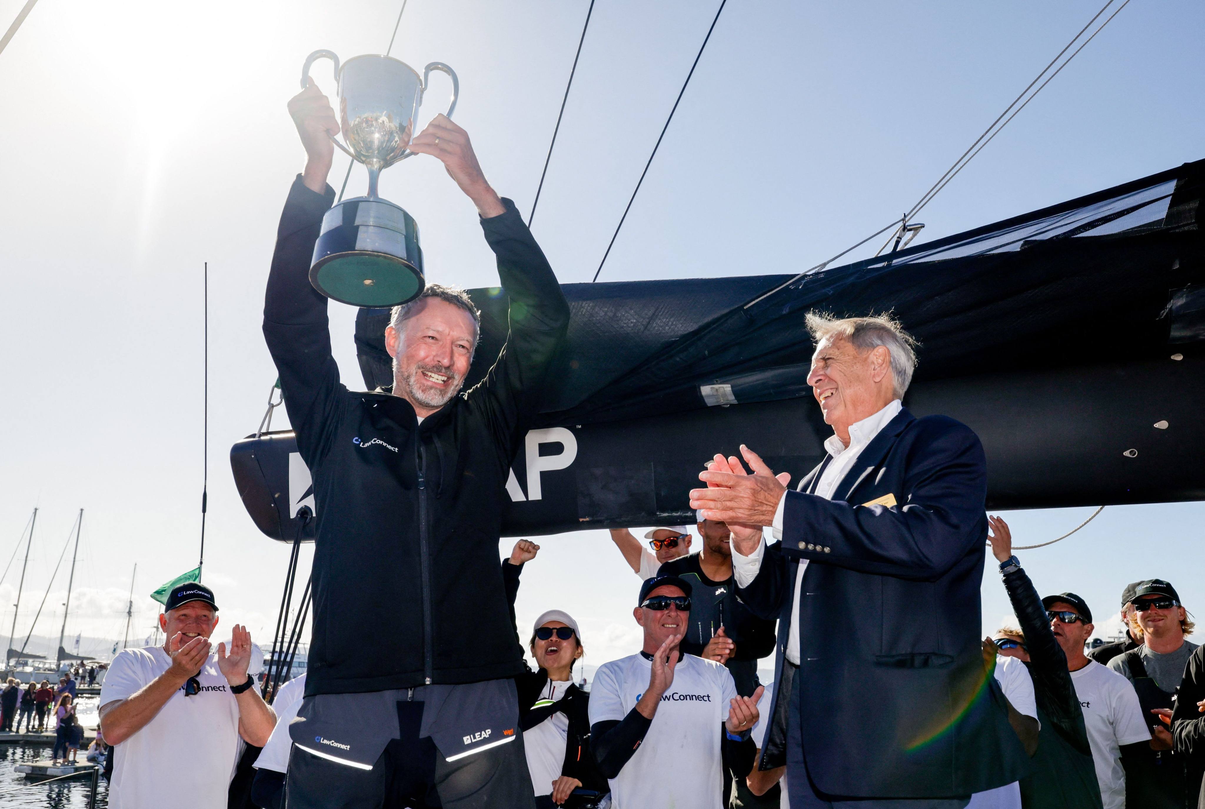 Christian Beck skipper and owner of LawConnect, lifts the John H. Illingworth Challenge Cup after being handed the trophy by Arthur Lane (right), the Commodore of the Cruising Yacht Club of Australia. Photo: AFP PHOTO/SALTY DINGO