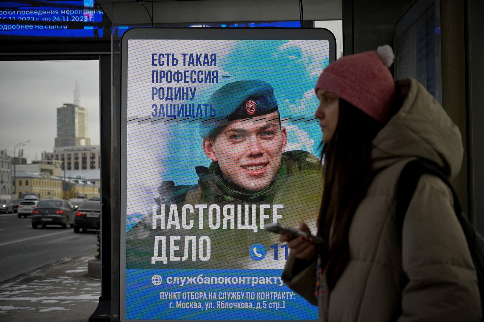 A woman waits at a Moscow bus stop with an advertising screen promoting contract military service in the Russian army. Photo: AFP via Getty Images / TNS