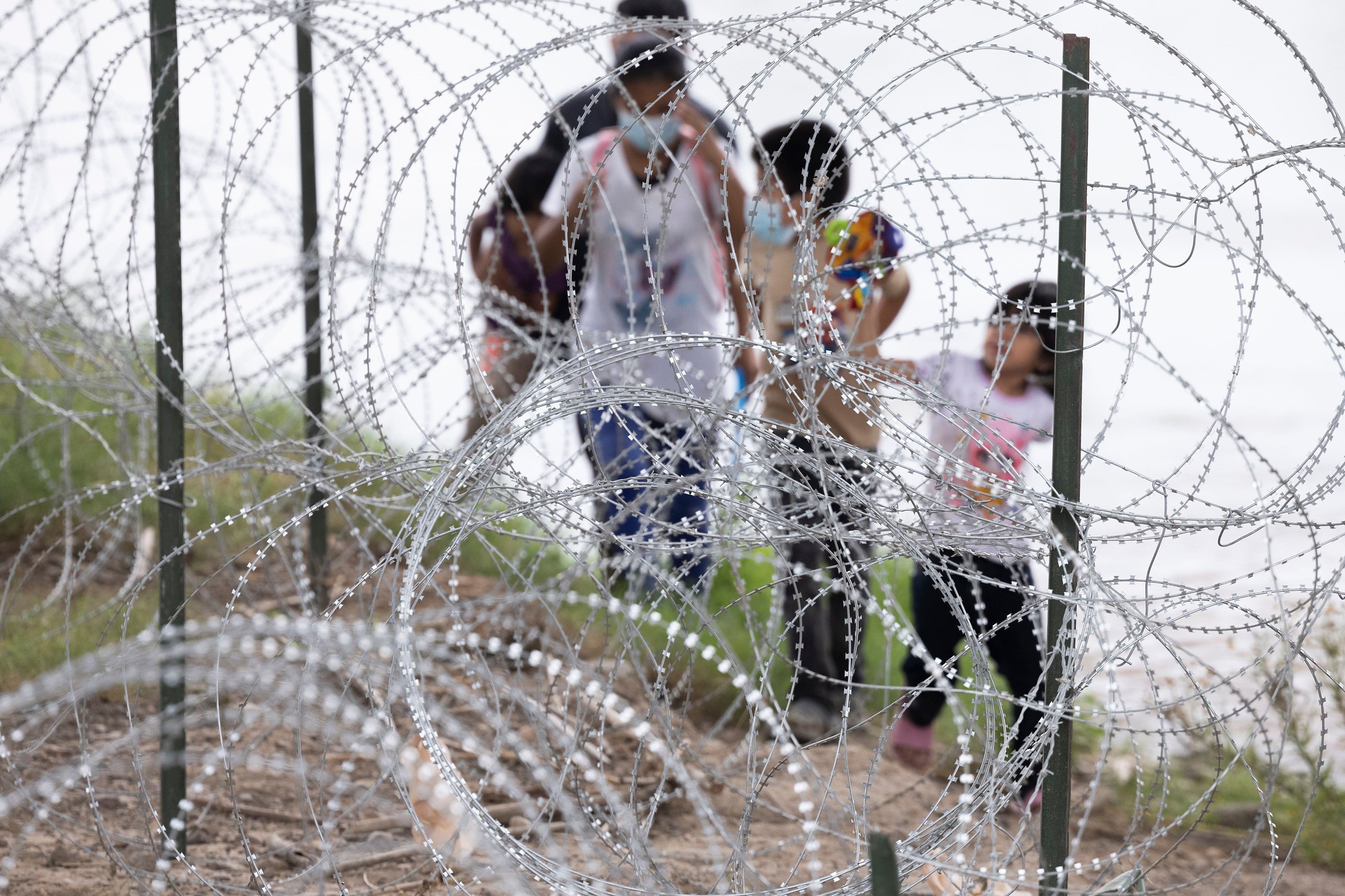 Migrants with children walk by razor wire fencing after crossing the Rio Grande River from Mexico into the US close to the Eagle Pass, Texas. Photo: The Dallas Morning News / TNS