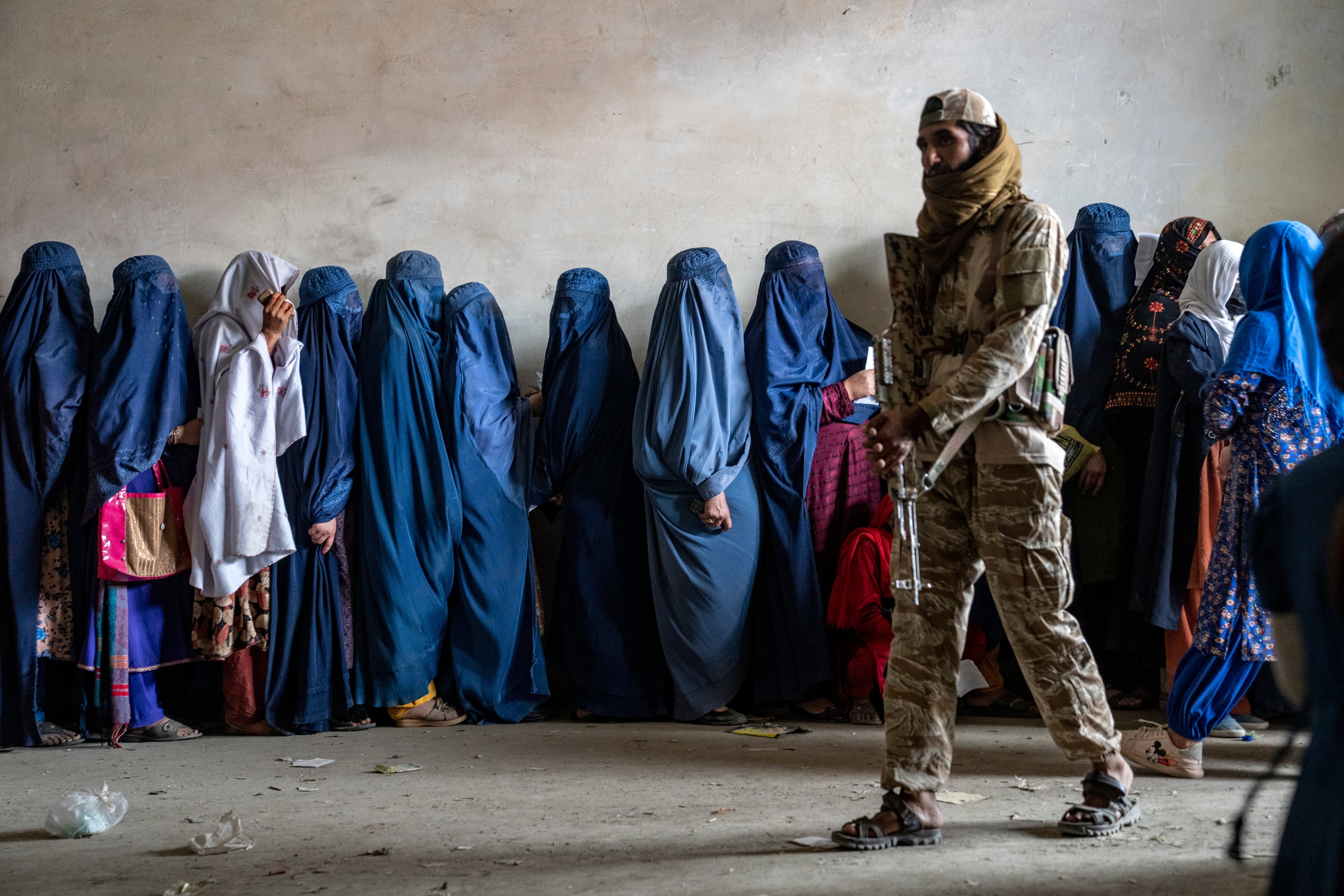 A Taliban fighter stands guard as women wait to receive food from a humanitarian aid group in Kabul on May 23. Photo: AP