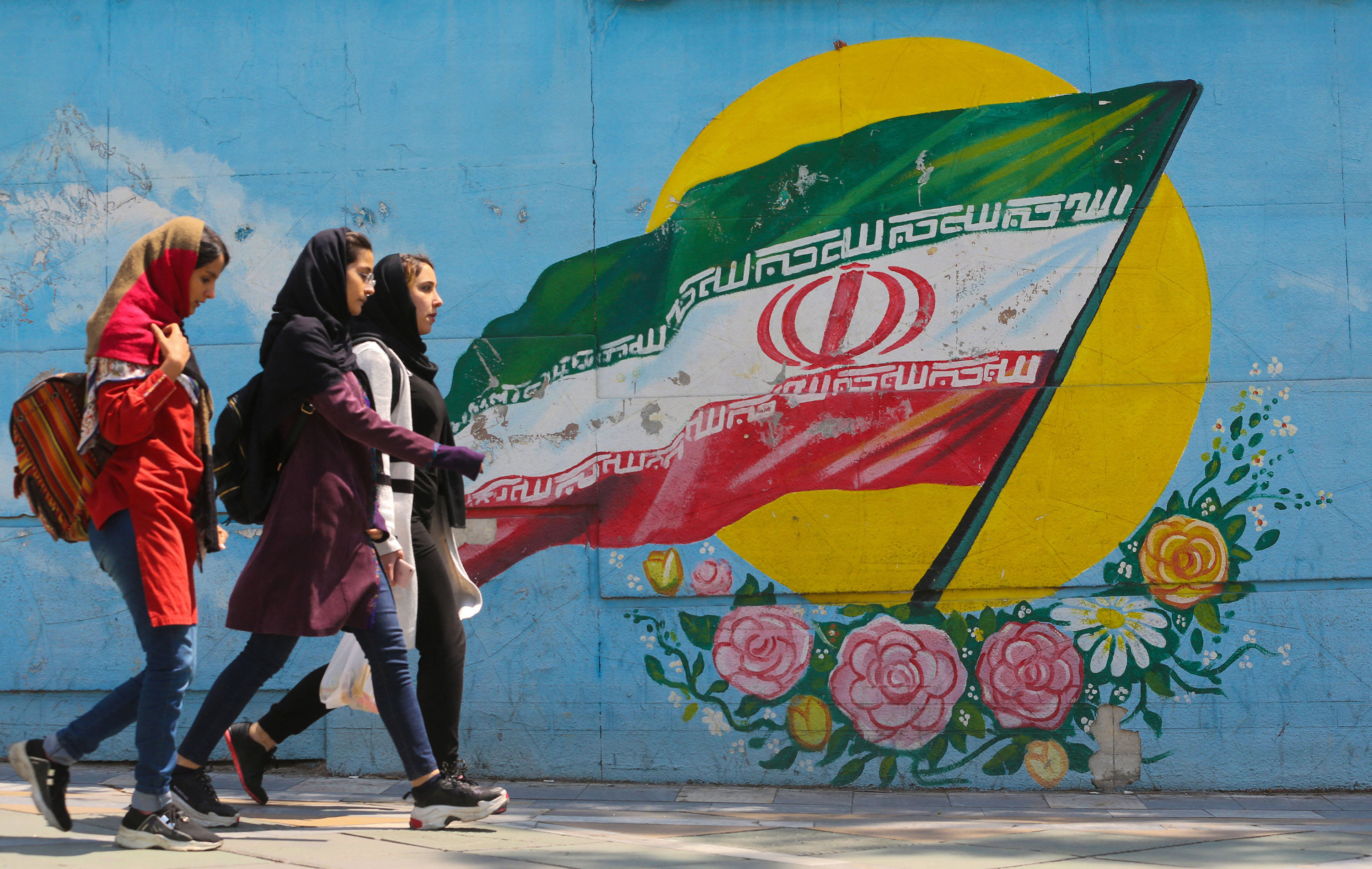 Young girls walk in front of a mural showing the Iranian national flag in the center of the  capital Tehran. Photo: TNS