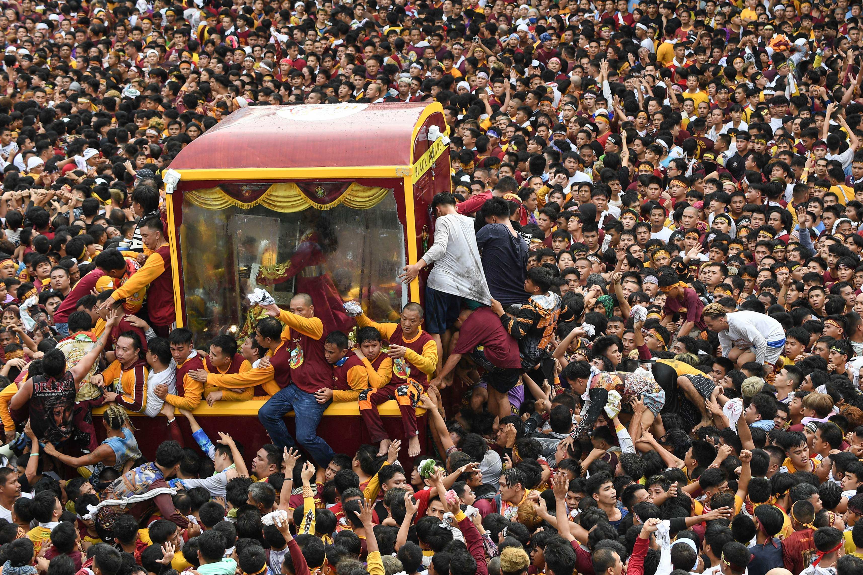 Catholic devotees climb  onto a glass-covered carriage carrying the so-called Black Nazarene statue as they try to touch it during a religious procession in Manila on Tuesday. Photo: AFP