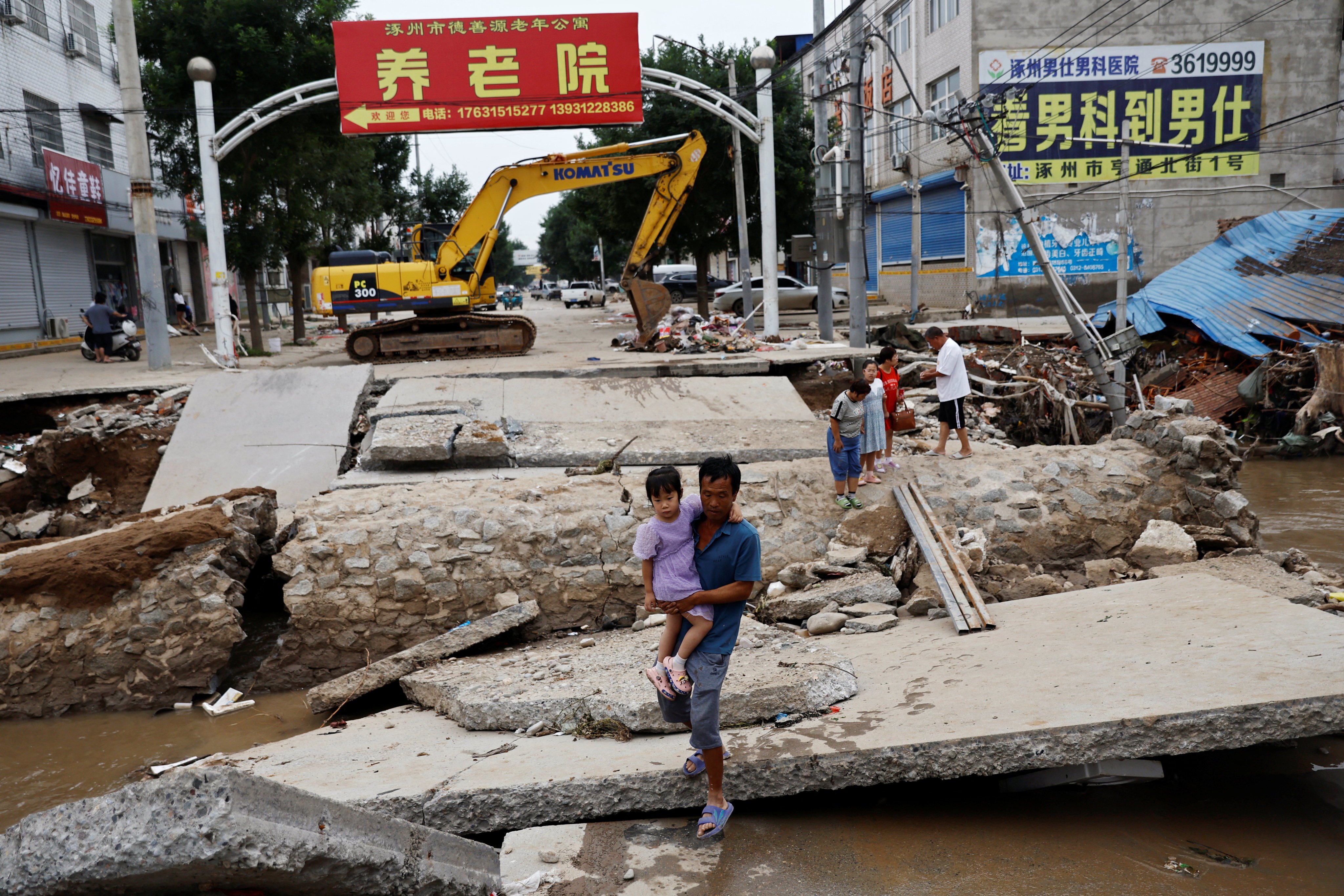 A man holding a child walks across a damaged bridge after rains and floods brought by remnants of Typhoon Doksuri, in Zhuozhou, Hebei province, China on August 7, 2023. Photo: Reuters