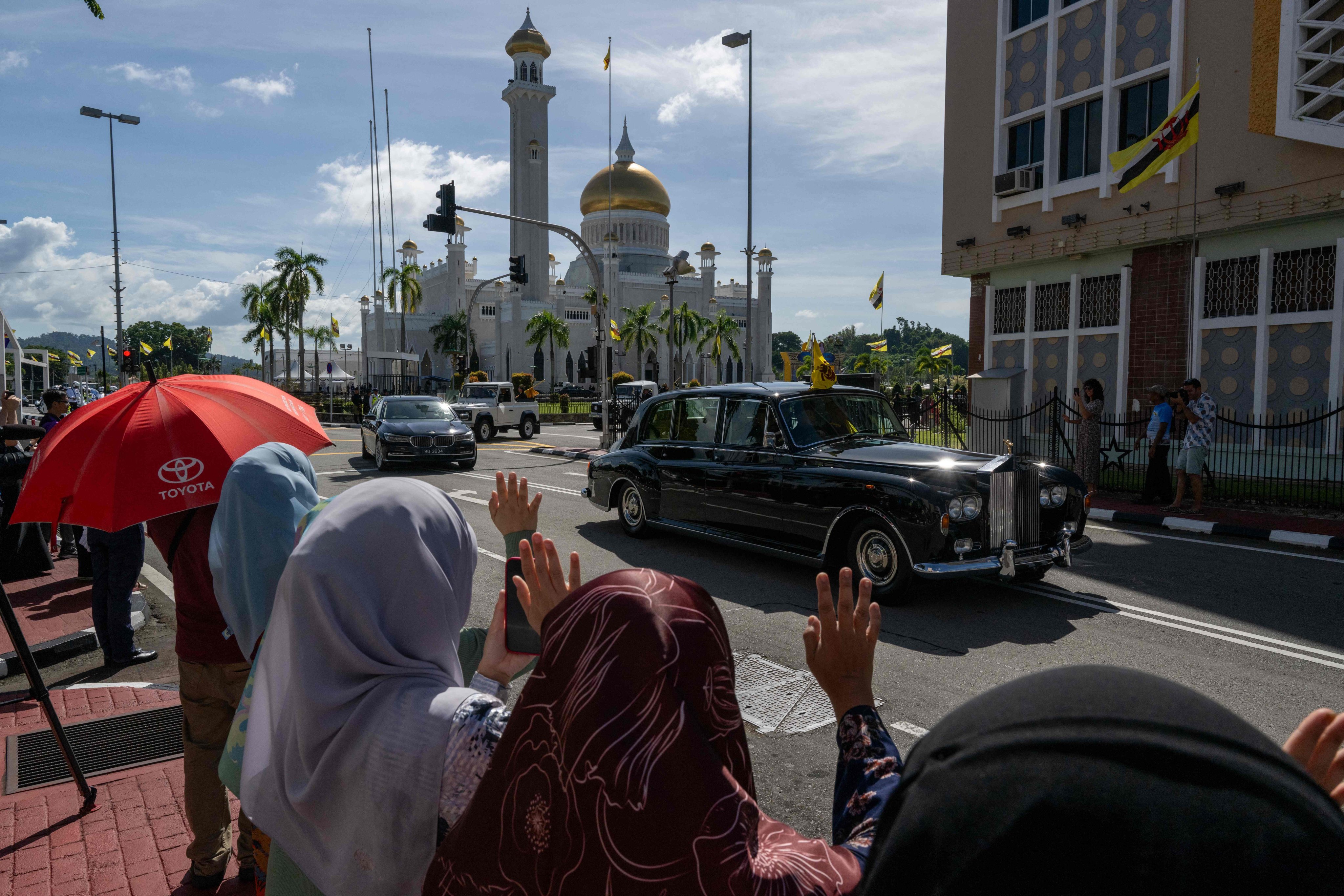 People wave to a car carrying Brunei’s Sultan Hassanal Bolkiah after his son’s wedding at the Sultan Omar Ali Saifuddien Mosque in Bandar Seri Begawan on Thursday. Photo: AFP