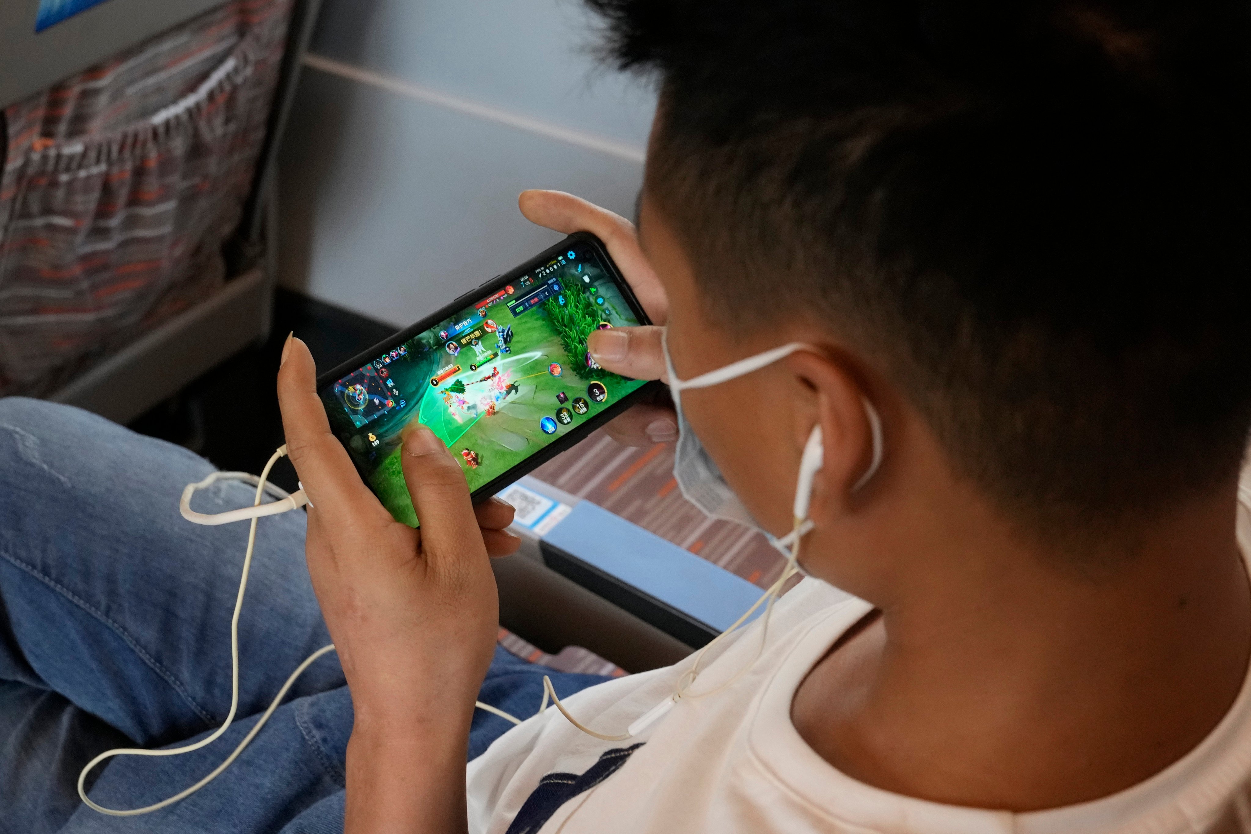 A man plays an online game from Tencent on a train. China released draft guidelines on December 22, 2023, aimed at curbing excessive spending on online gaming. Photo: AP