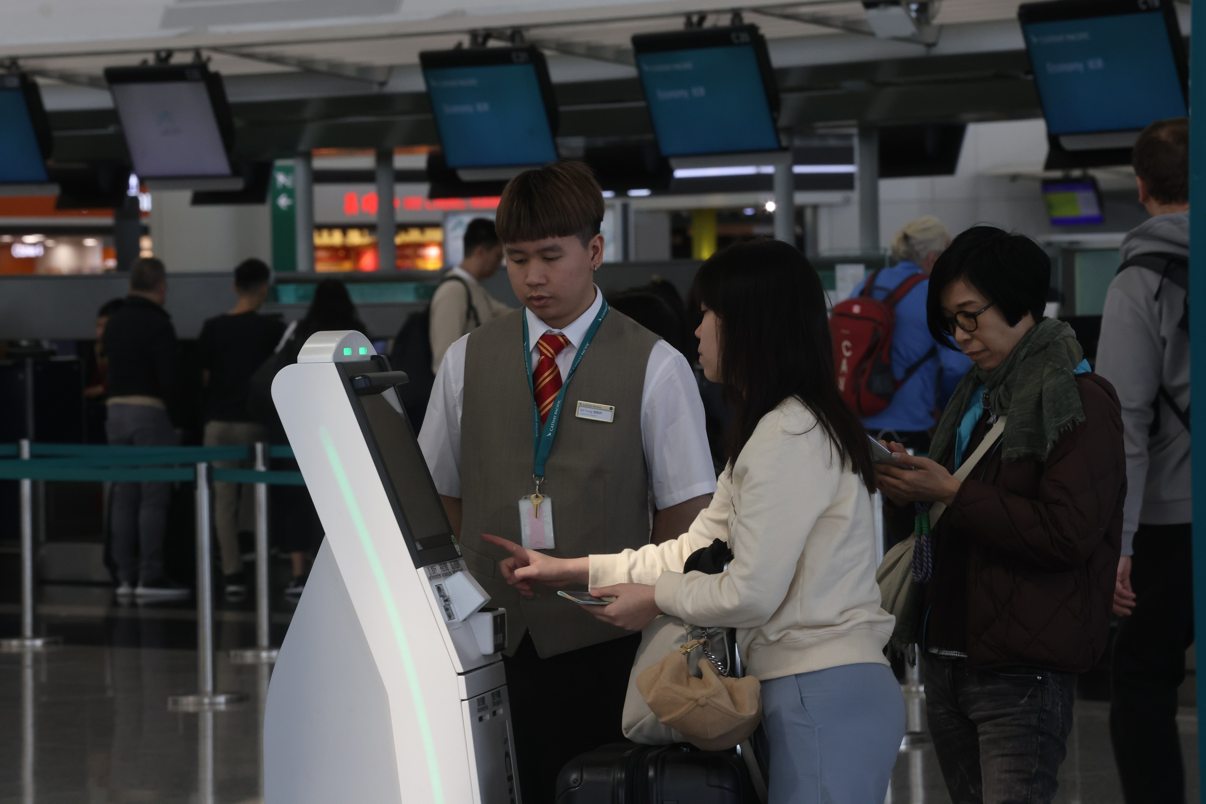 A Cathay Pacific staff member helps passengers check in for their flights at a kiosk at Hong Kong International Airport on January 12. Cathay passengers have expressed frustration with the airline after a series of flight cancellations that the airline blamed on a lack of staffing because of an influenza outbreak. Photo: Jonathan Wong
