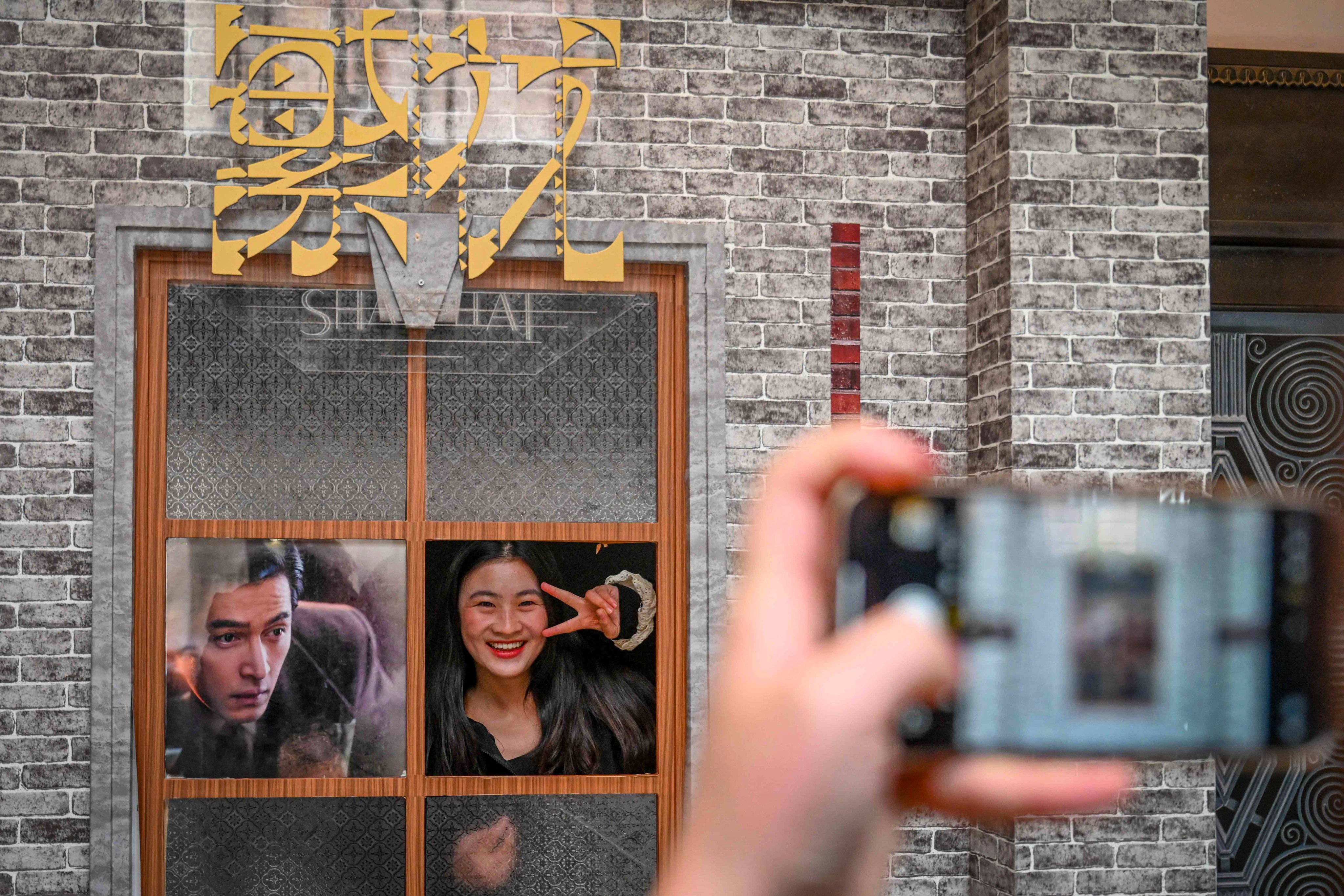 A woman poses for photos next to a poster for the new hit TV show ‘Blossoms Shanghai’, set in gritty but glamourous 1990s Shanghai. Photo: AFP