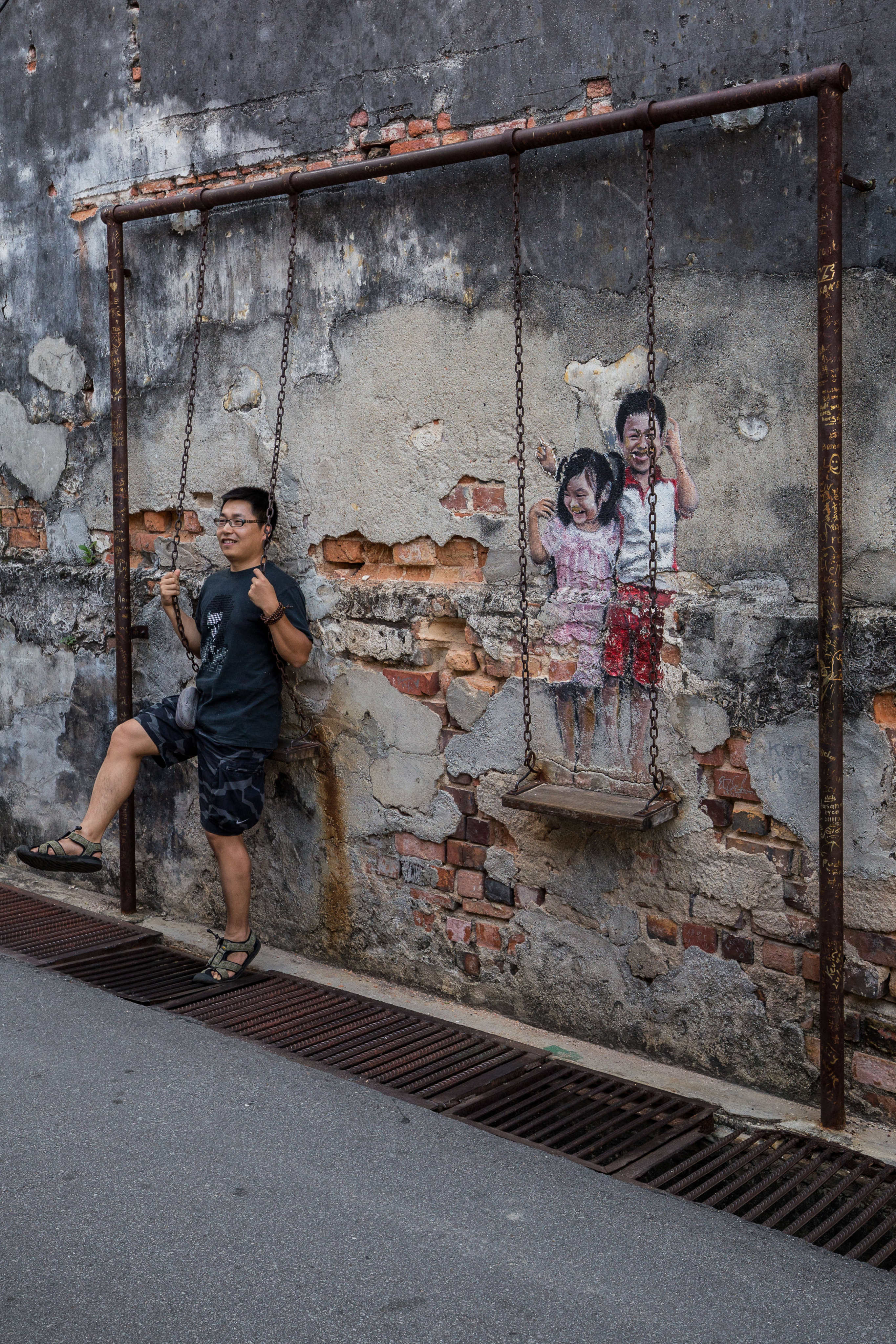A tourist has his photo taken next to “Brother and Sister on a Swing”, a work of street art in George Town, Penang, Malaysia, by local artist Louis Gan. Photo: Getty Images