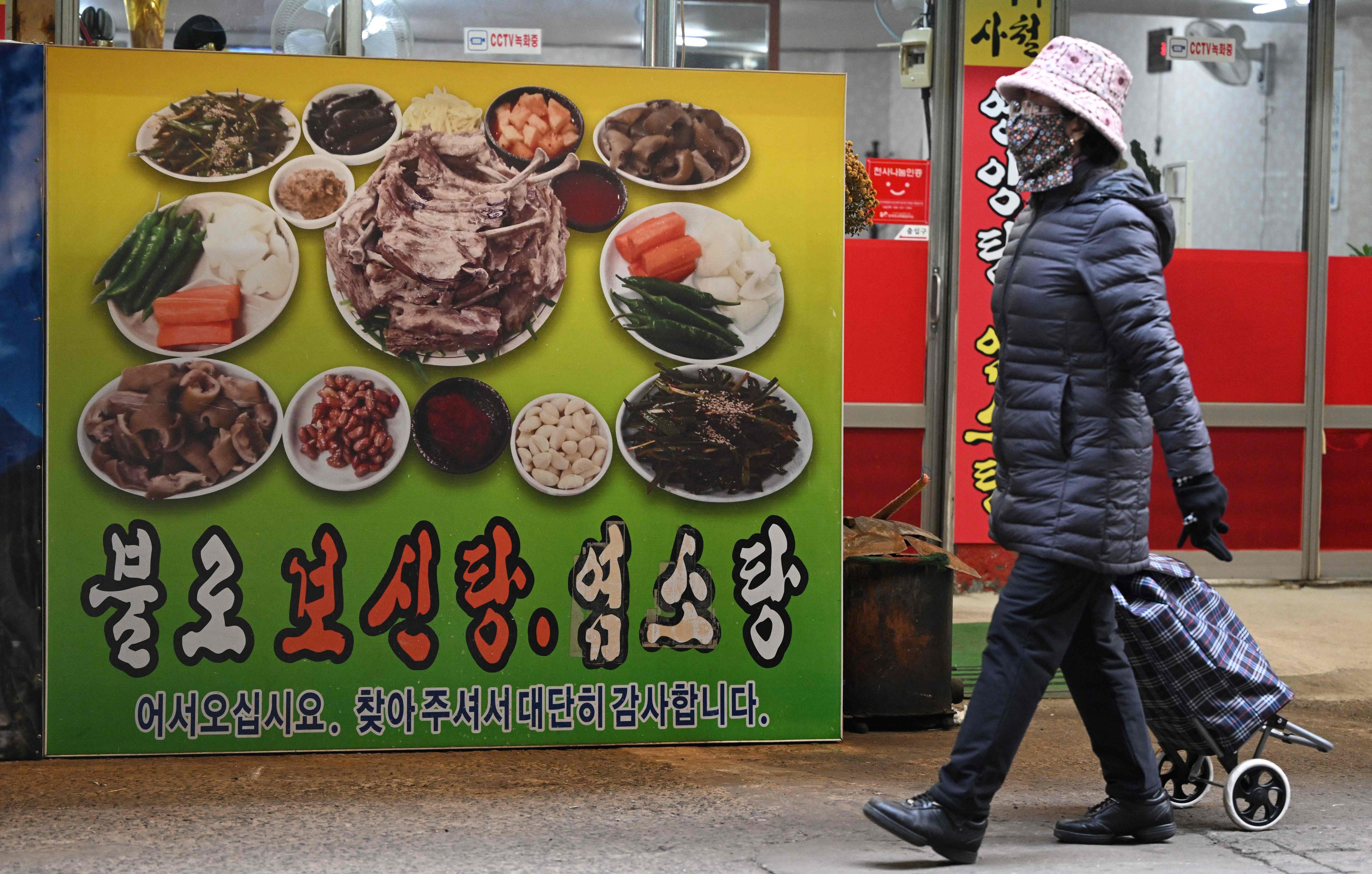 A woman walks in front of a poster advertising dog meat dishes in Daegu on January 10. Photo: AFP 