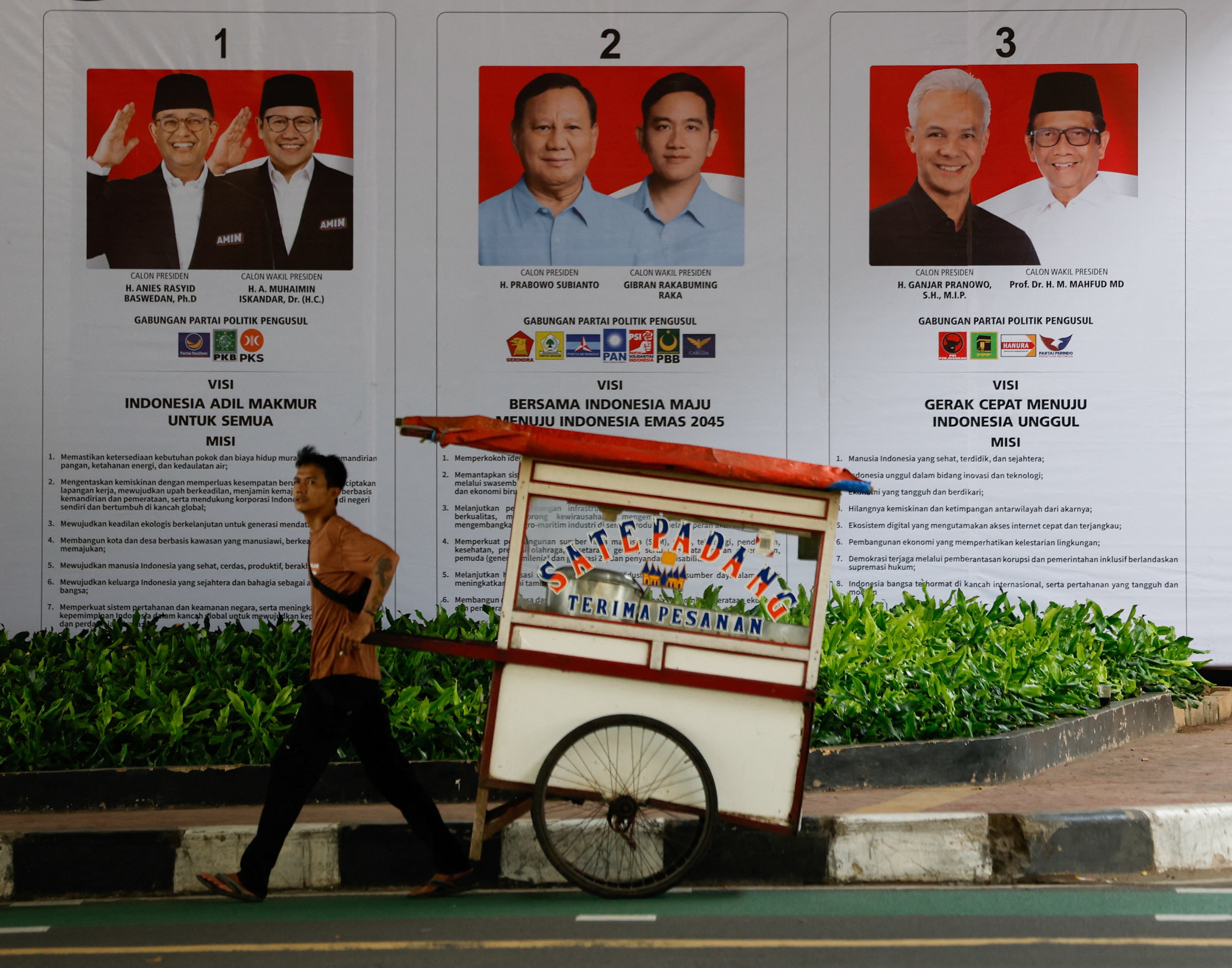 A street vendor pulls his cart past a banner showing presidential candidates contesting the upcoming general election in Jakarta, Indonesia, on Saturday. Photo: Reuters