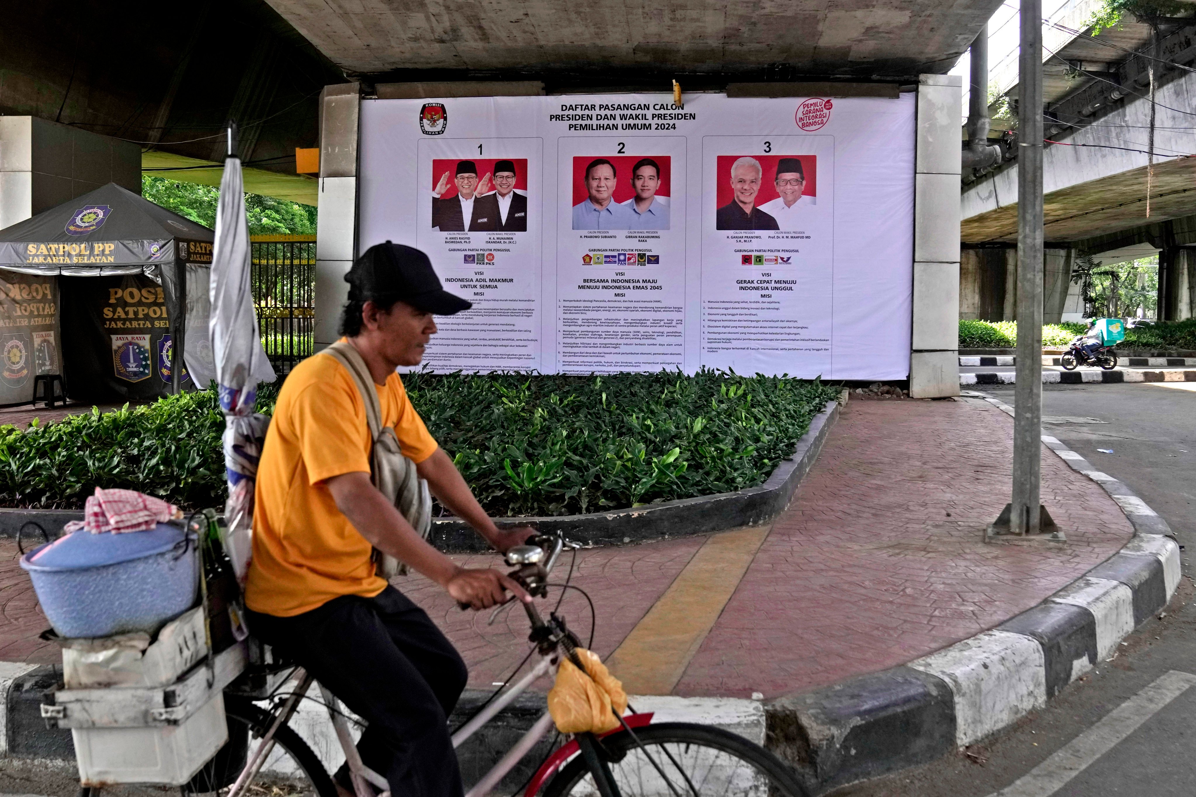 A food vendor rides his bicycle past a General Election Commission’s banner showing the photos of presidential candidates in Jakarta. Photo: AP