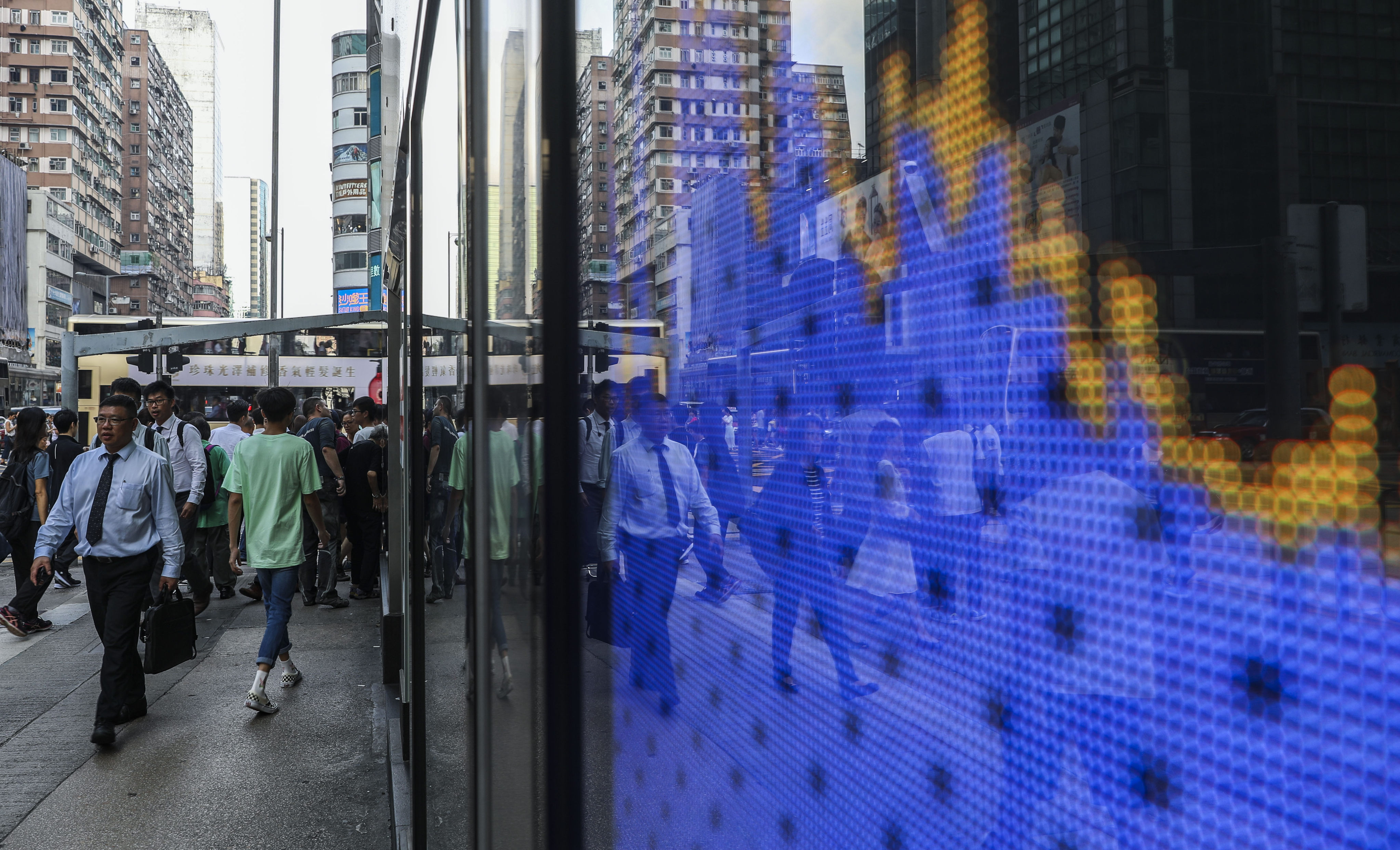 People walking near a screen showing the Hang Seng Index chart outside a bank branch in Mong Kok, hong Kong. Photo: Sam Tsang