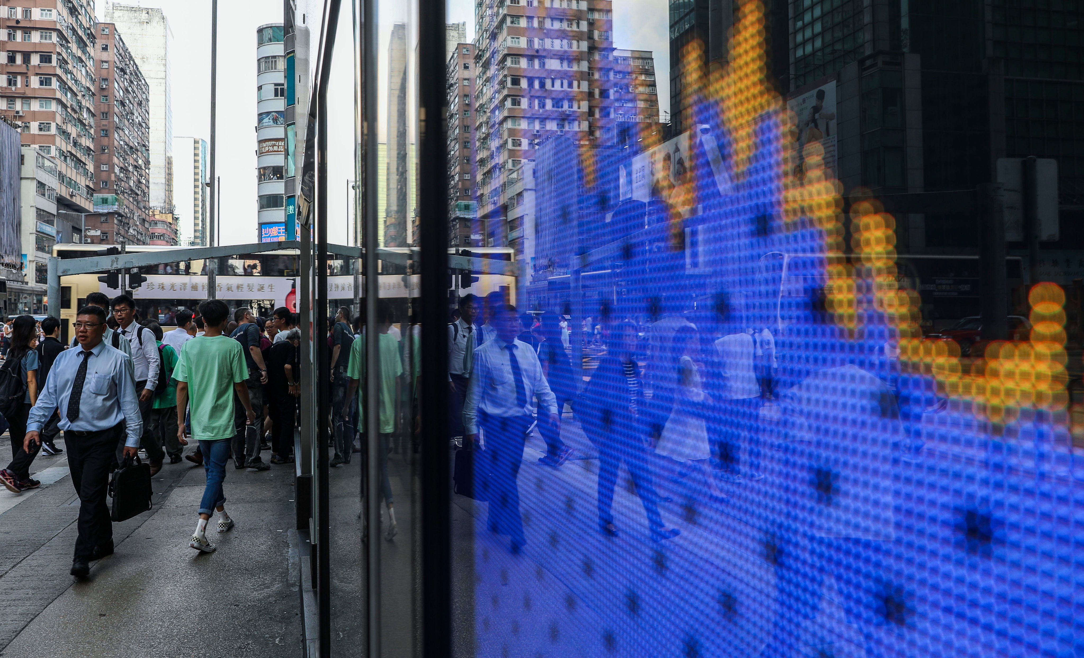 People walking near a screen showing the Hang Seng Index chart outside a bank branch in Mong Kok, hong Kong. Photo: Sam Tsang