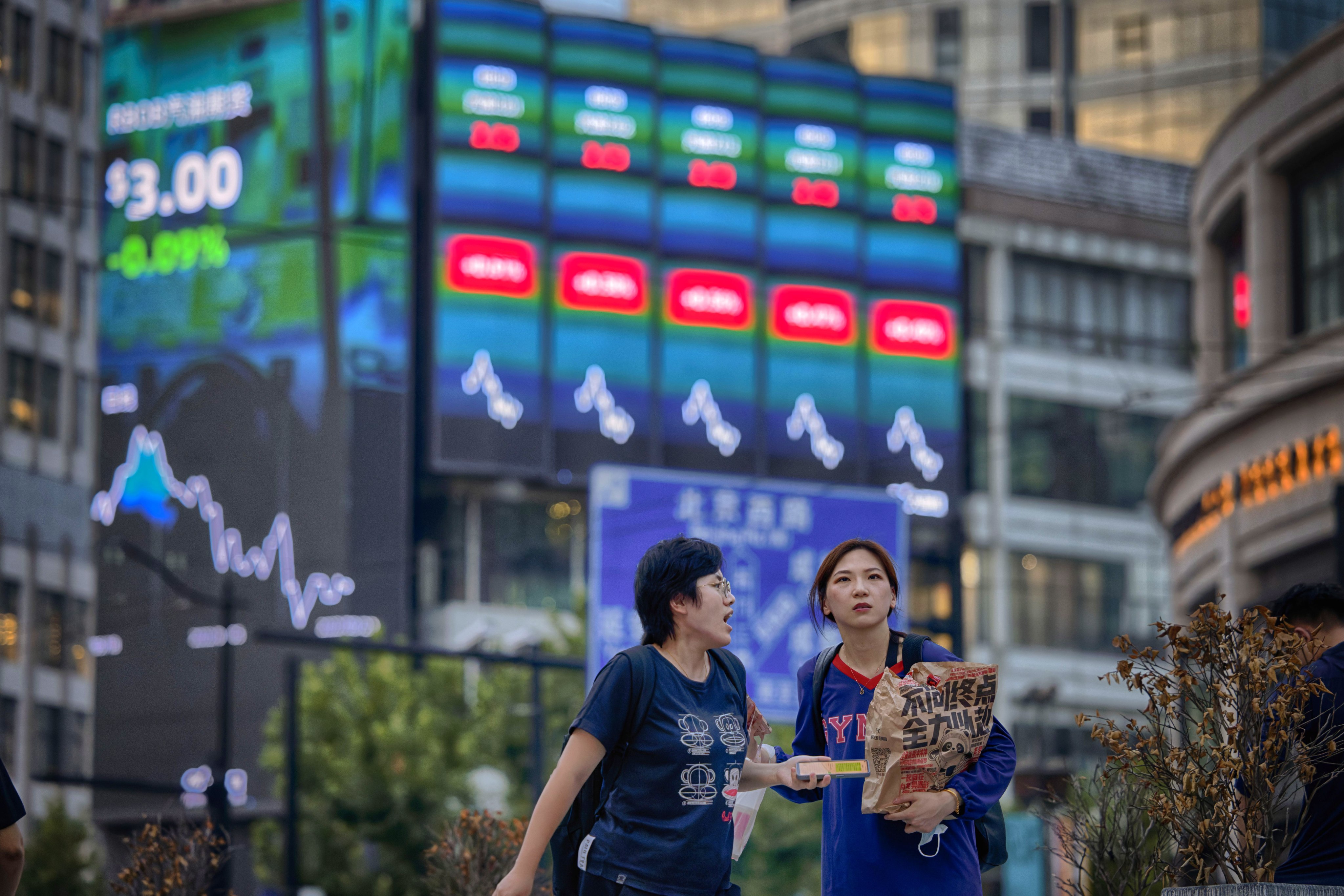 People walk in front of a large screen showing stock exchange data in Shanghai, China in 2022. Photo: EPA/EFE