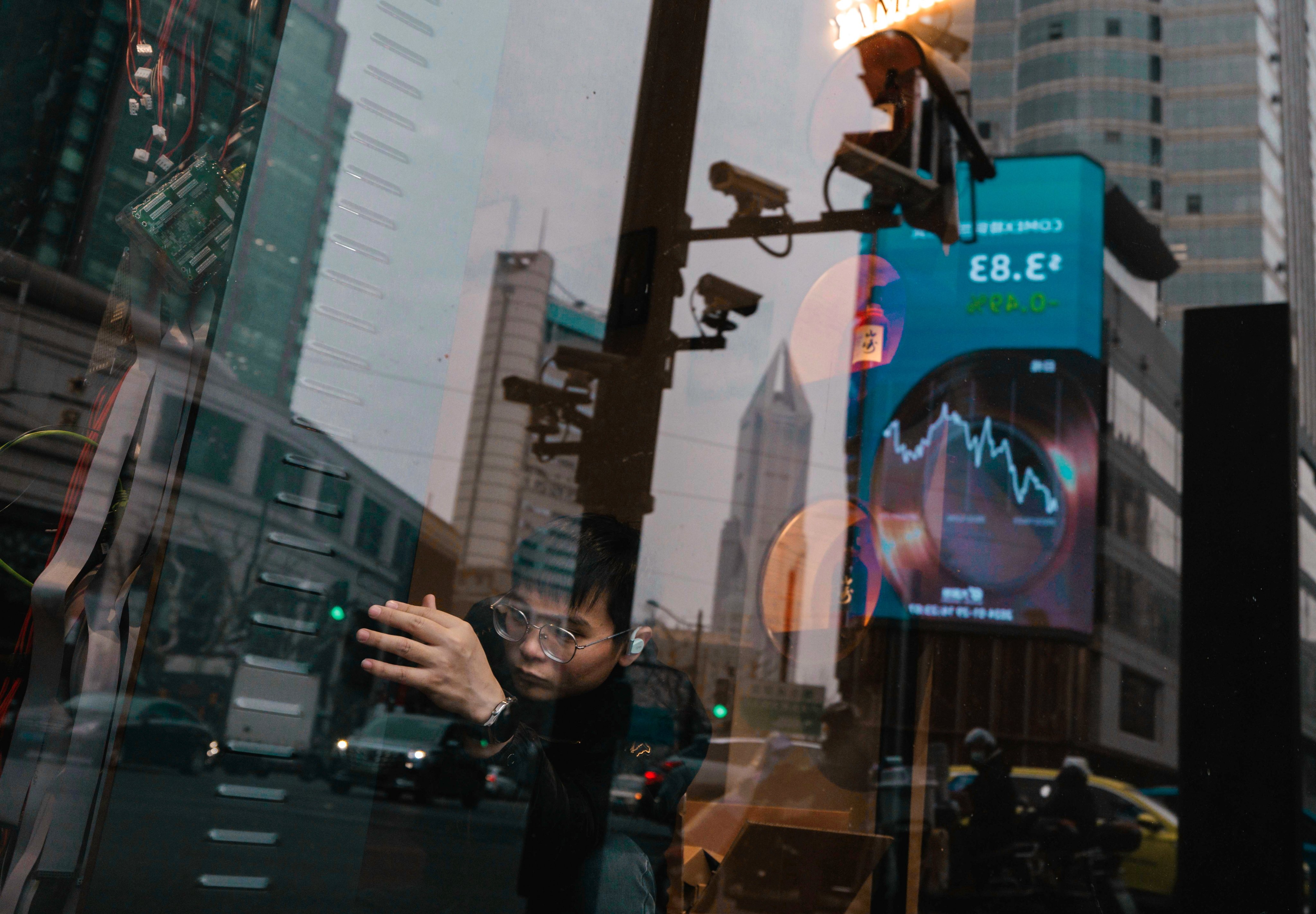  A man works in a shop while a large screen showing the latest stock exchange and economic data is seen reflected on the window in Shanghai on January 29. Photo: EPA-EFE