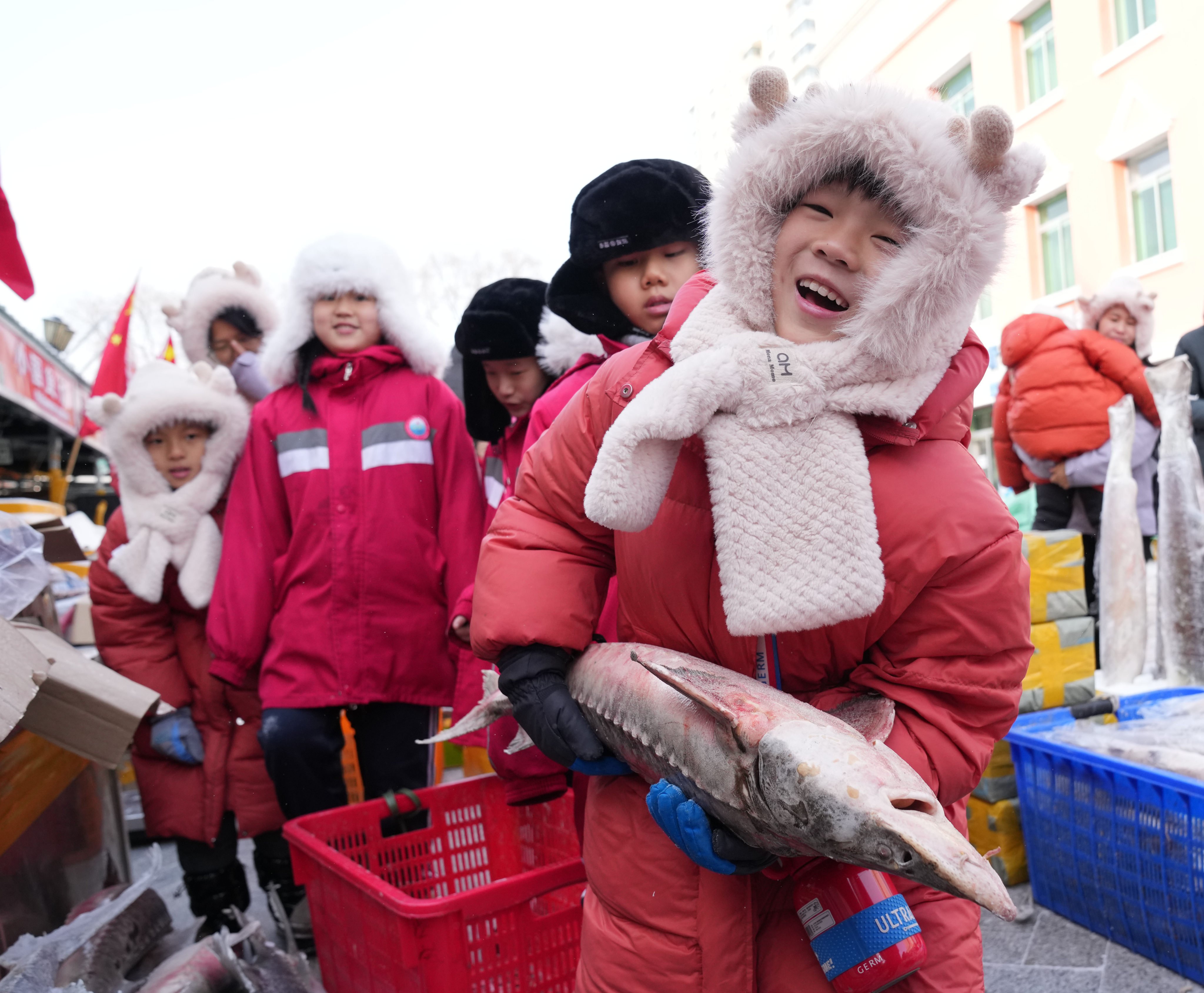 A child from Guangdong holds a fish at a market in Fuyuan, in northeast China’s Heilongjiang province, on January 29. Fuyuan is hosting a group of children from the southern province for a study tour, alongside local children, during the winter holiday. Photo: Xinhua