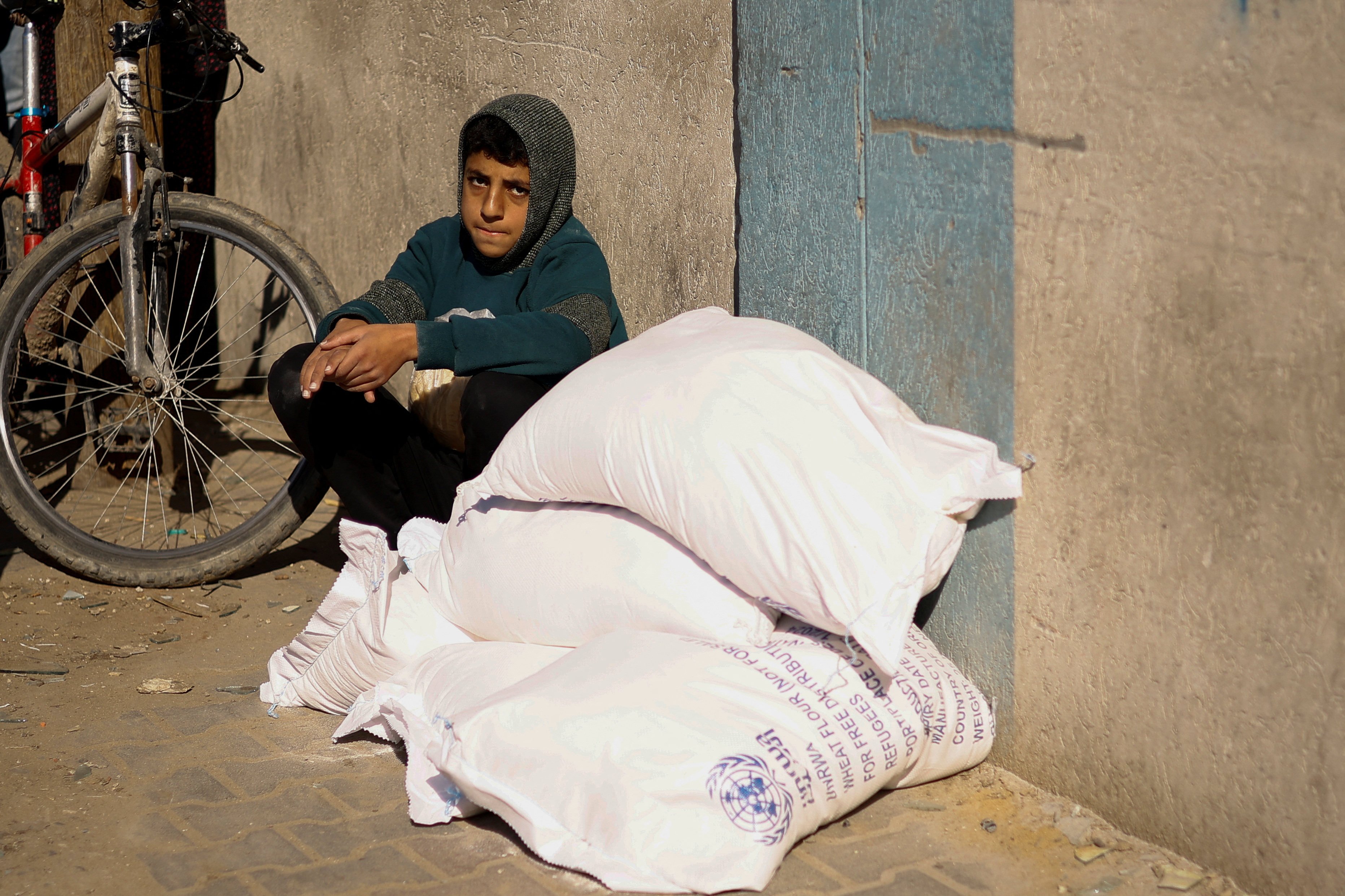 A Palestinian youth sits next to bags of flour distributed by the United Nations Relief and Works Agency (UNRWA), amid the ongoing conflict between Israel and Palestinian Islamist group Hamas. Photo: Reuters
