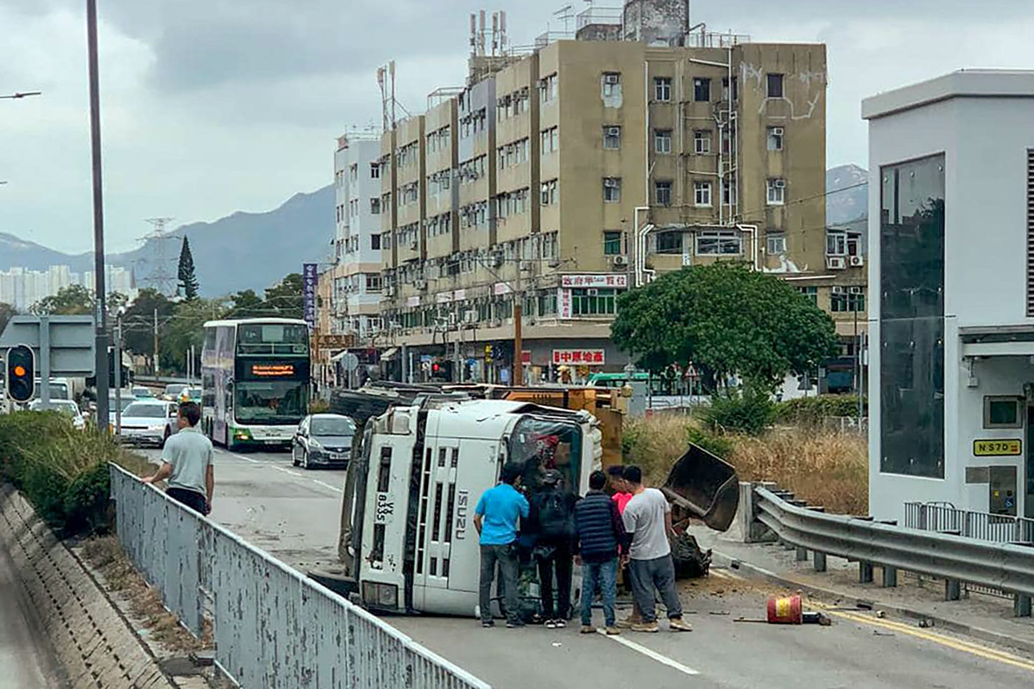 Passers-by mount a rescue bid after a truck hit a central divider and overturned, trapping its driver inside. Photo: Facebook/@車cam L