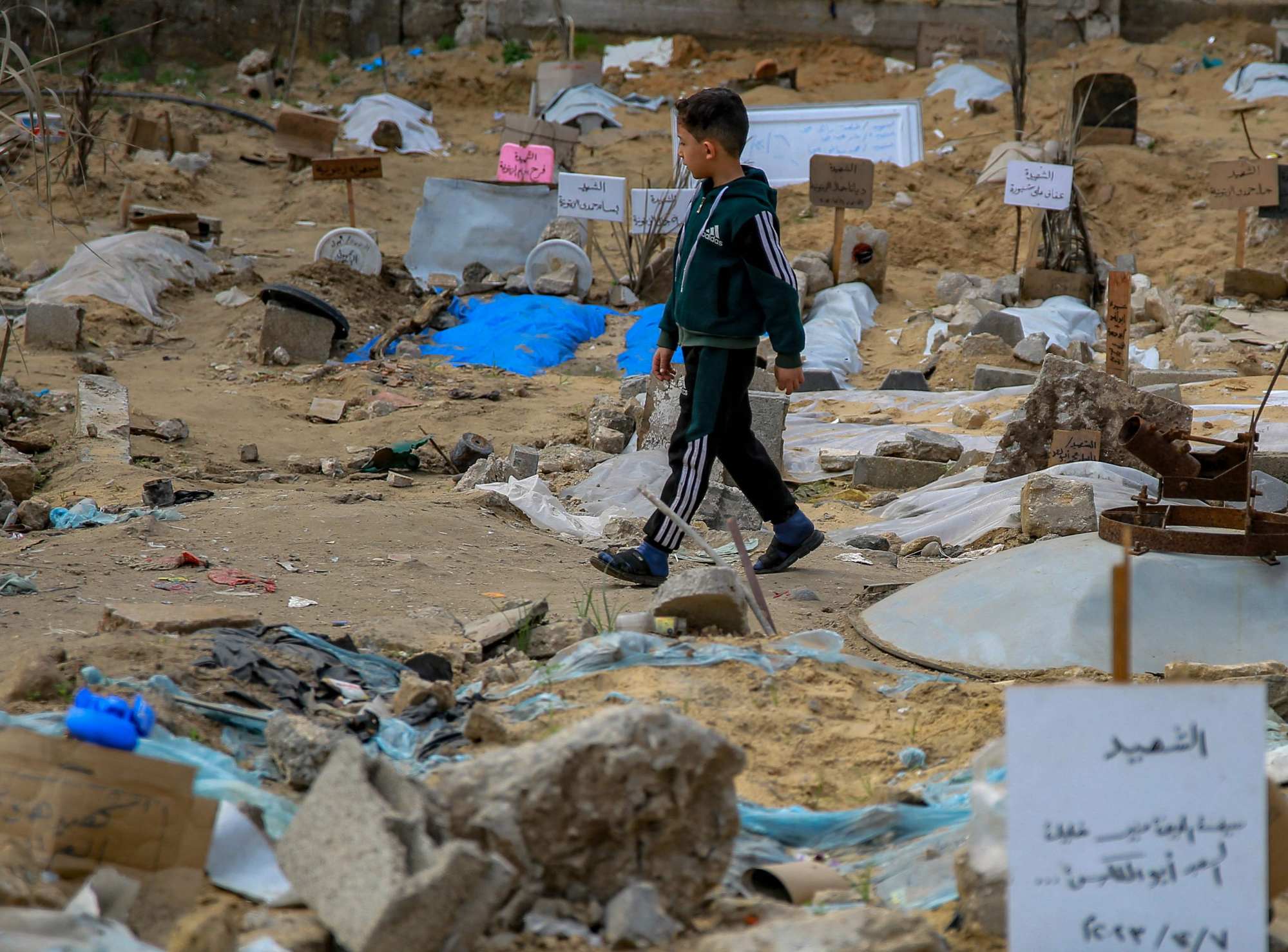 A Palestinian boy walks inside a makeshift cemetery where people killed in Israeli bombing are buried in shallow tombs, in Gaza City’s Al-Sahaba Street. Photo: AFP