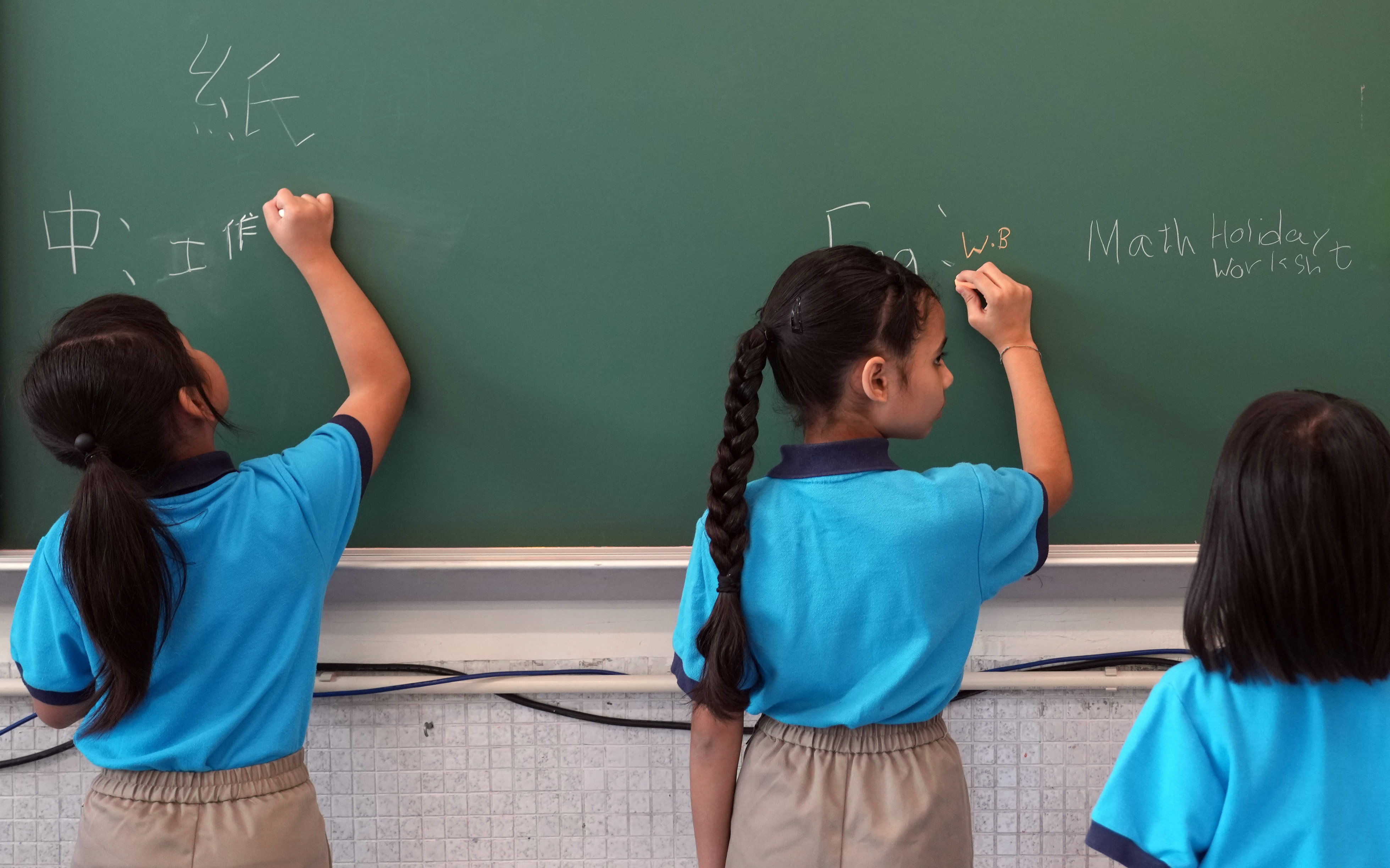 Pupils write on the chalkboard on the first day of the new school year at the Tsuen Wan Trade Association Primary School in Tsing Yi on September 4, 2023. Language barriers and other difficulties have held back those from ethnic minority communities from fully integrating into Hong Kong. Photo: Sam Tsang