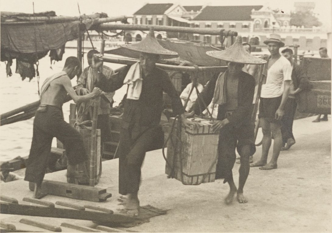 Stevedores at the wharf, circa 1900s. Stevedores have long played a crucial role as an essential workforce in the freight transport industry. From the 19th century, they toiled daily in harsh weather conditions, shouldering goods and shuttling between barges, ocean liners, and bustling docks, relying on crude gangplanks. Photo courtsey of Mr Dennis George Crow Dennis George Crow