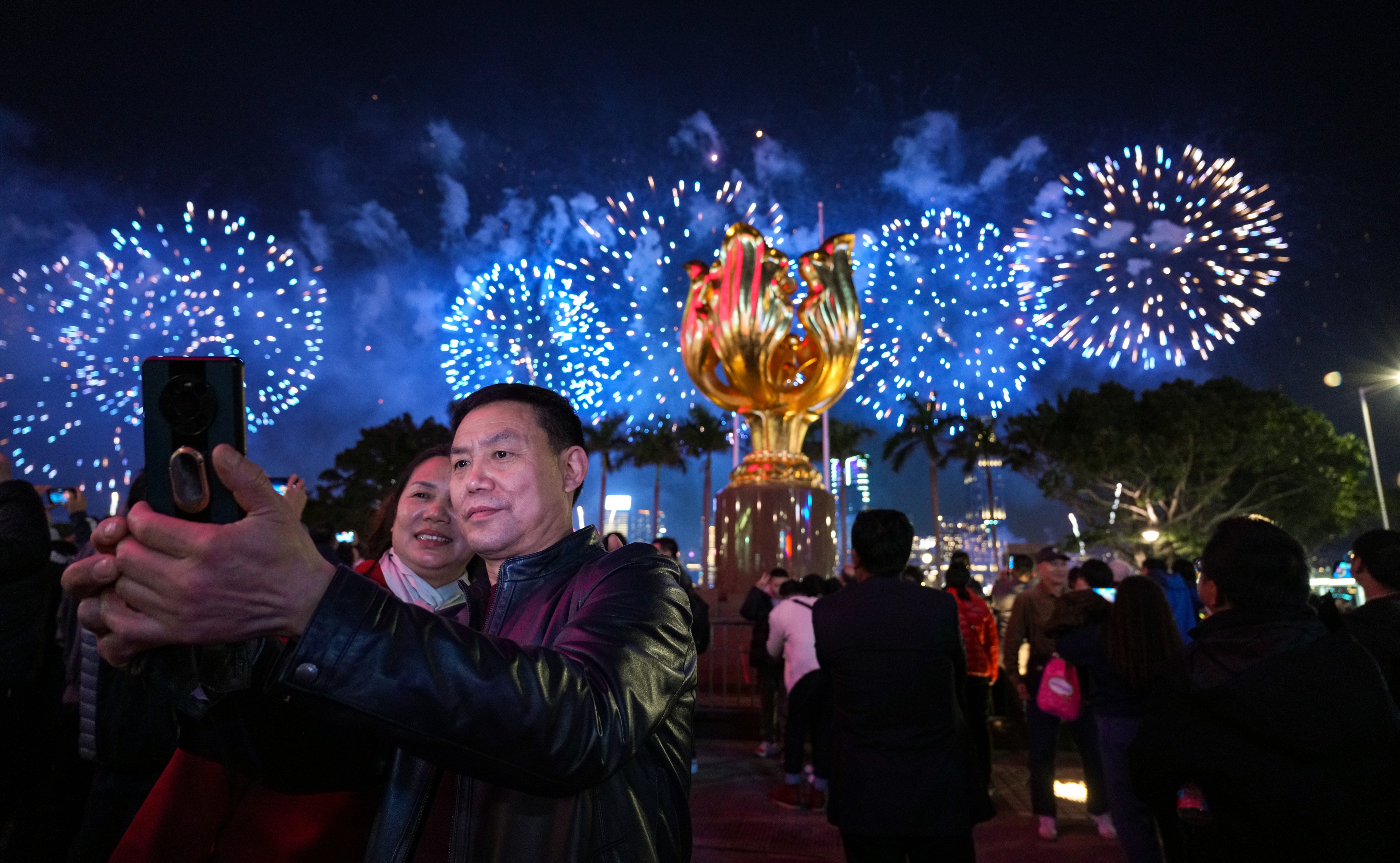 Visitors take a photograph, with a fireworks display to celebrate the Lunar New Year in the background, at Golden Bauhinia Squre in Wan Chai on February 11. Photo: Eugene Lee