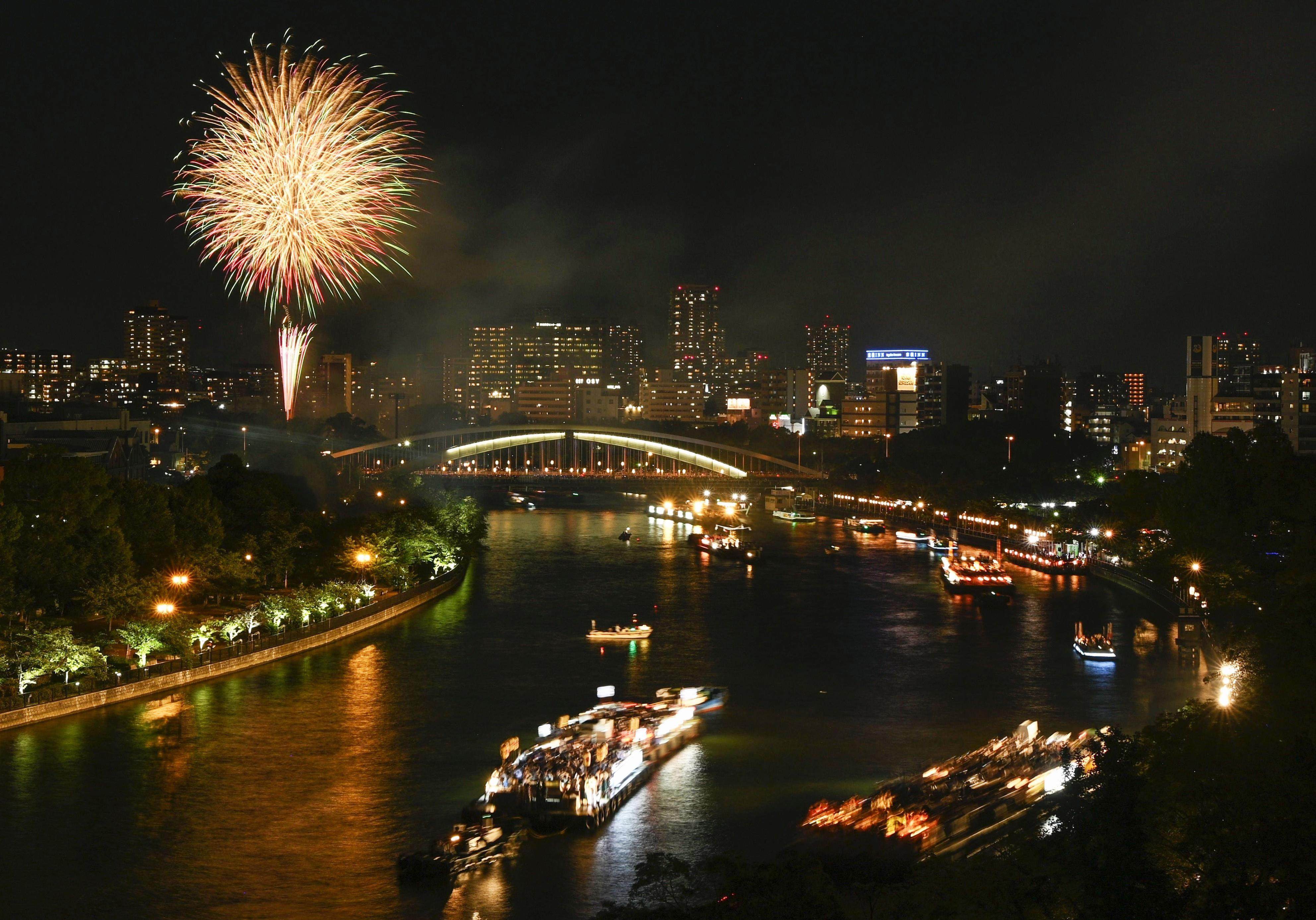 Boats sail along a river in Osaka, Japan during the Tenjin Festival on July 25, 2023, with fireworks lighting up the night sky. Photo: Kyodo