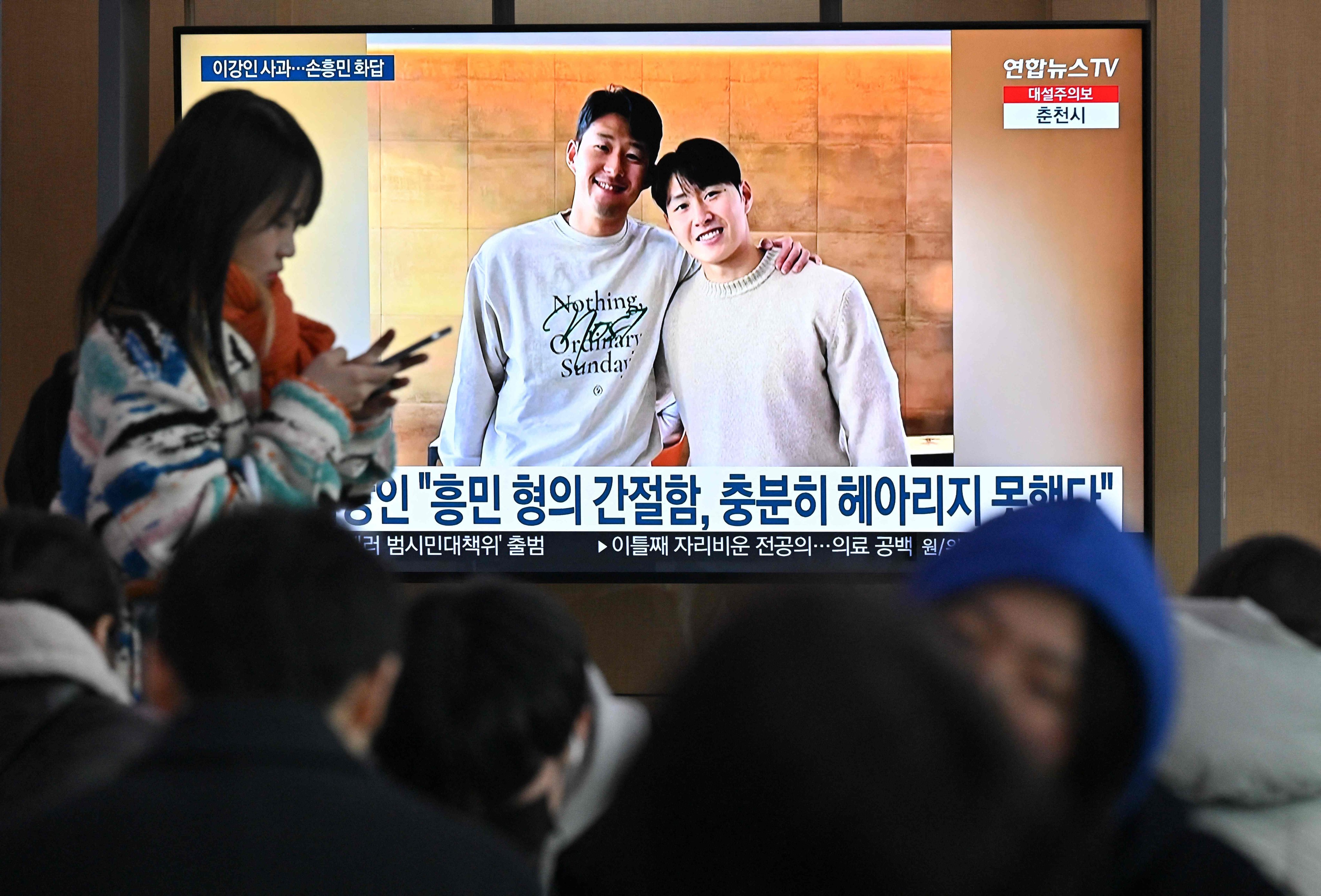 A woman walks past a television screen showing a news broadcast with a picture of Son Heung-min (L) and Lee Kang-in (R), at a railway station in Seoul on February 21, 2024. Son Heung-min apologised on February 21, for his role in a bust-up with South Korea team-mate Lee Kang-in at the Asian Cup and urged fans to forgive the Paris Saint-Germain player. (Photo by Jung Yeon-je / AFP)