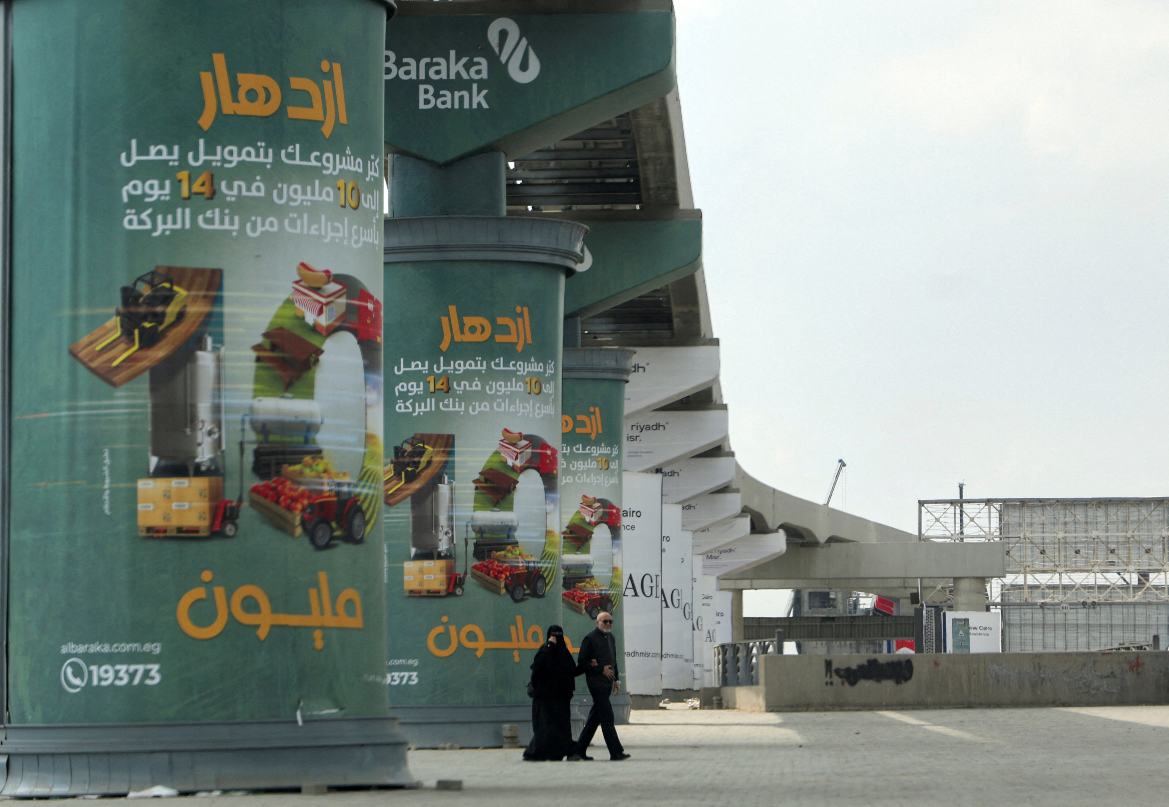 An Egyptian couple walks next to advertising credit investment certificates by a branch of Al Baraka Bank on walls of a new monorail line in Cairo, Egypt, on March 7. Photo: Reuters
