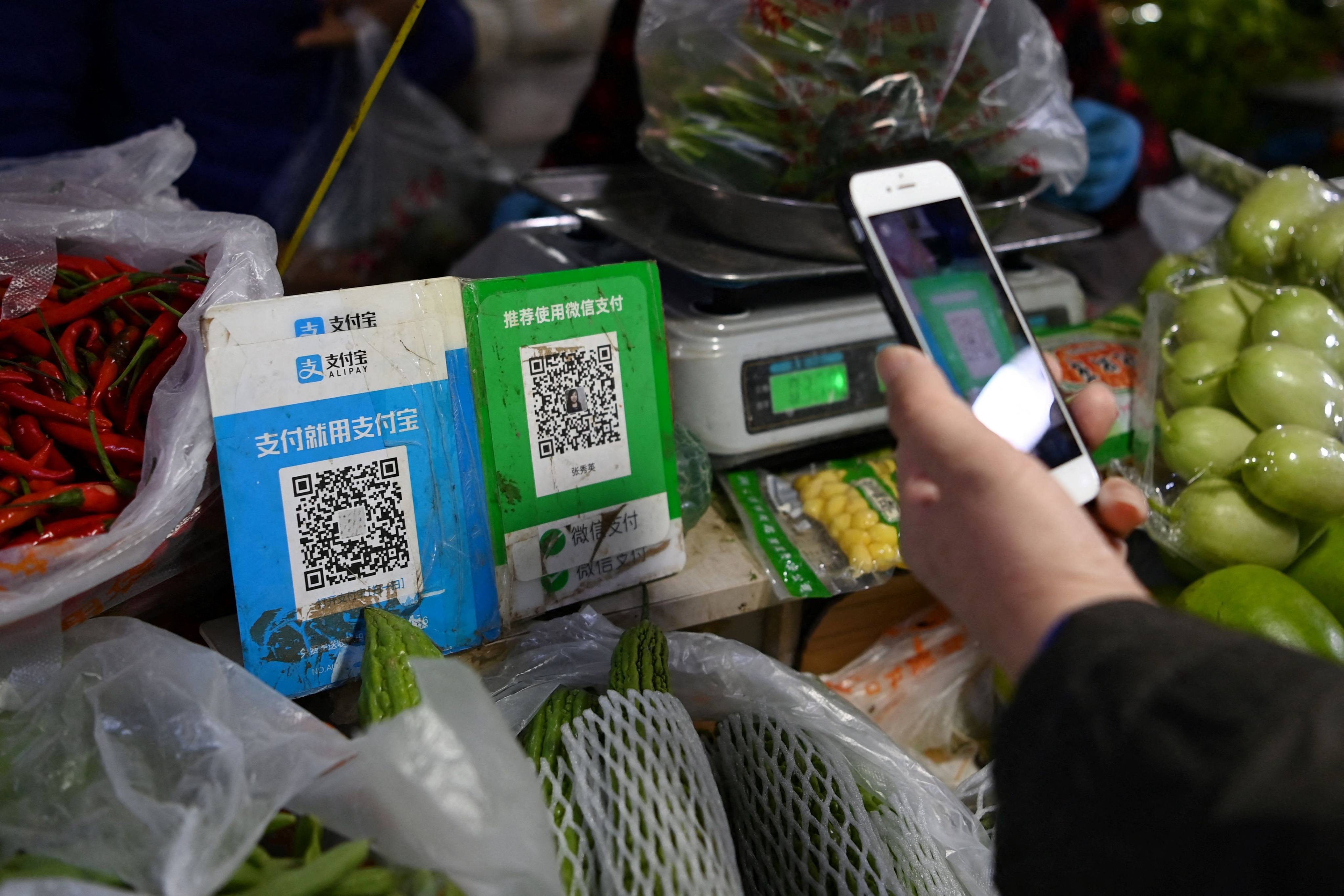 A customer buys produce using a WeChat QR payment code with her smartphone next to an Alipay QR code in Beijing on November 3, 2020. Photo: AFP