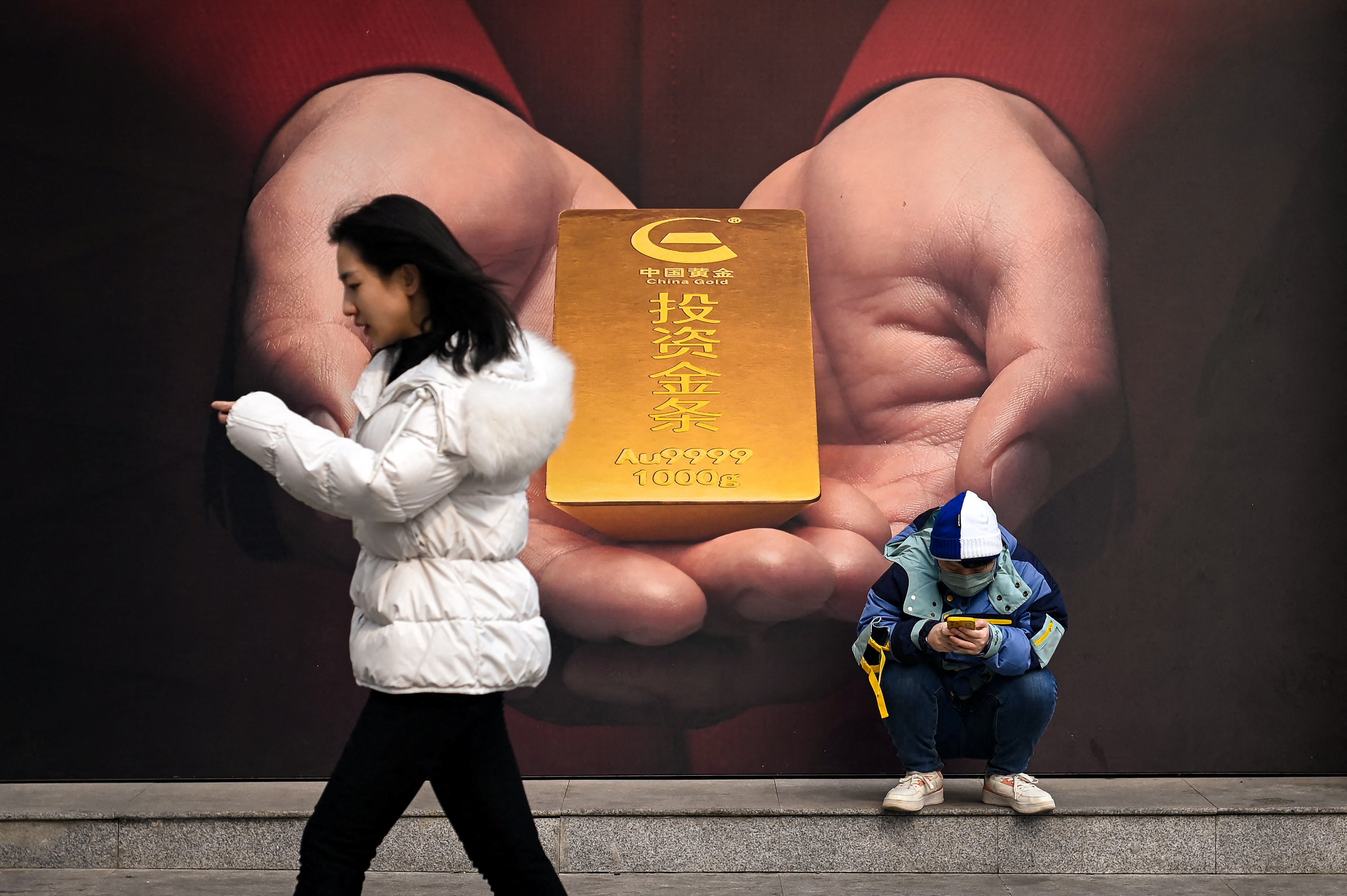 A man uses his mobile phone in front of a poster of gold along a street in Beijing, China. Photo: AFP