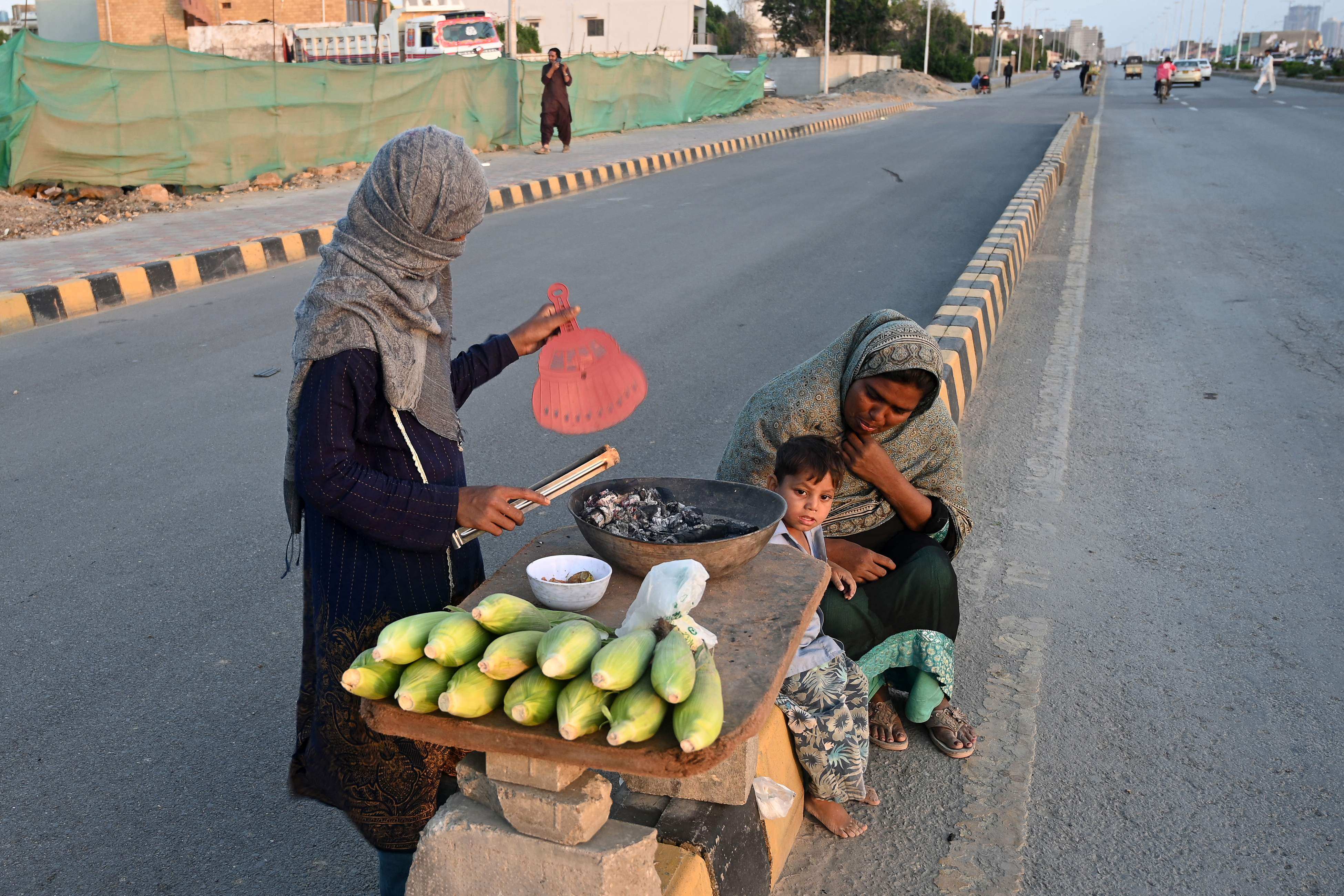 Women selling roasted corn wait for customers along the road in Karachi, Pakistan, on March 6. Photo: AFP