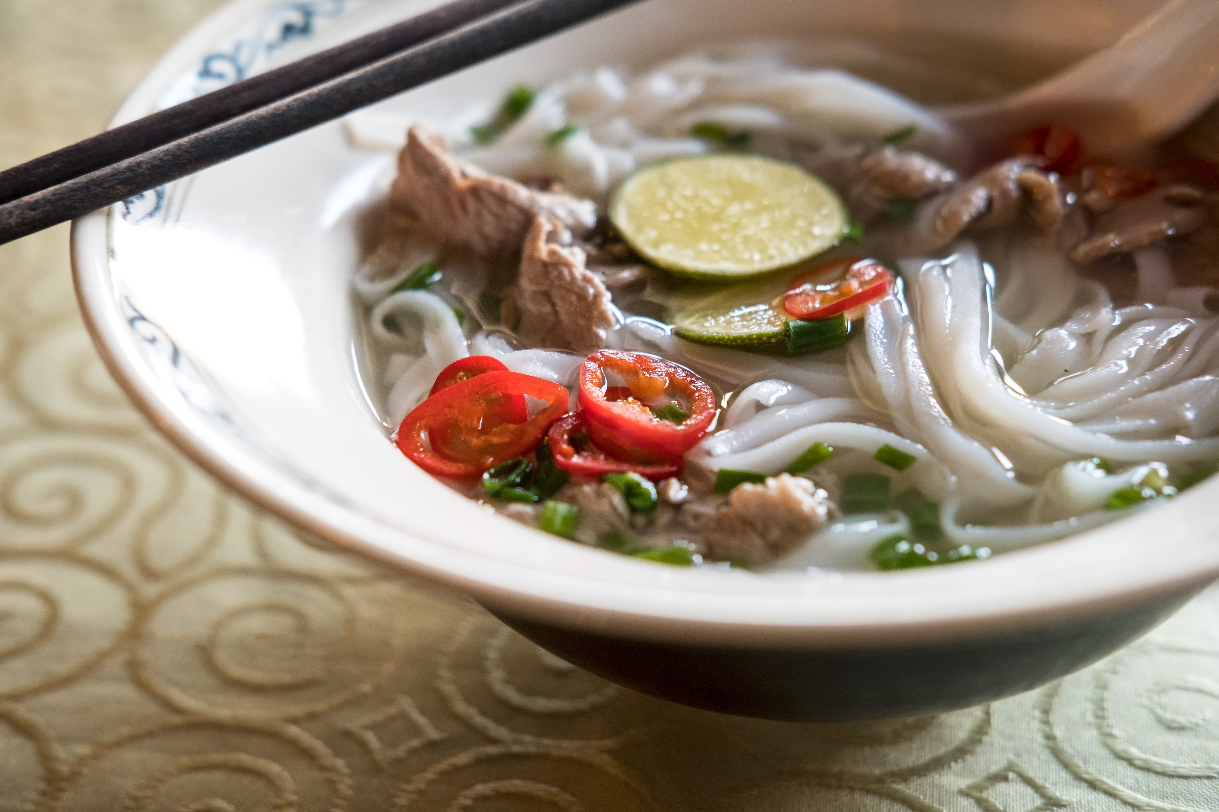 Regional Food Elements and Background:  Pho Bo - authentic Vietnamese Beef Noodle Soup served in Hanoi, Vietnam with typical garnishes served on an elegant embrodered tablecloth. Getty mages